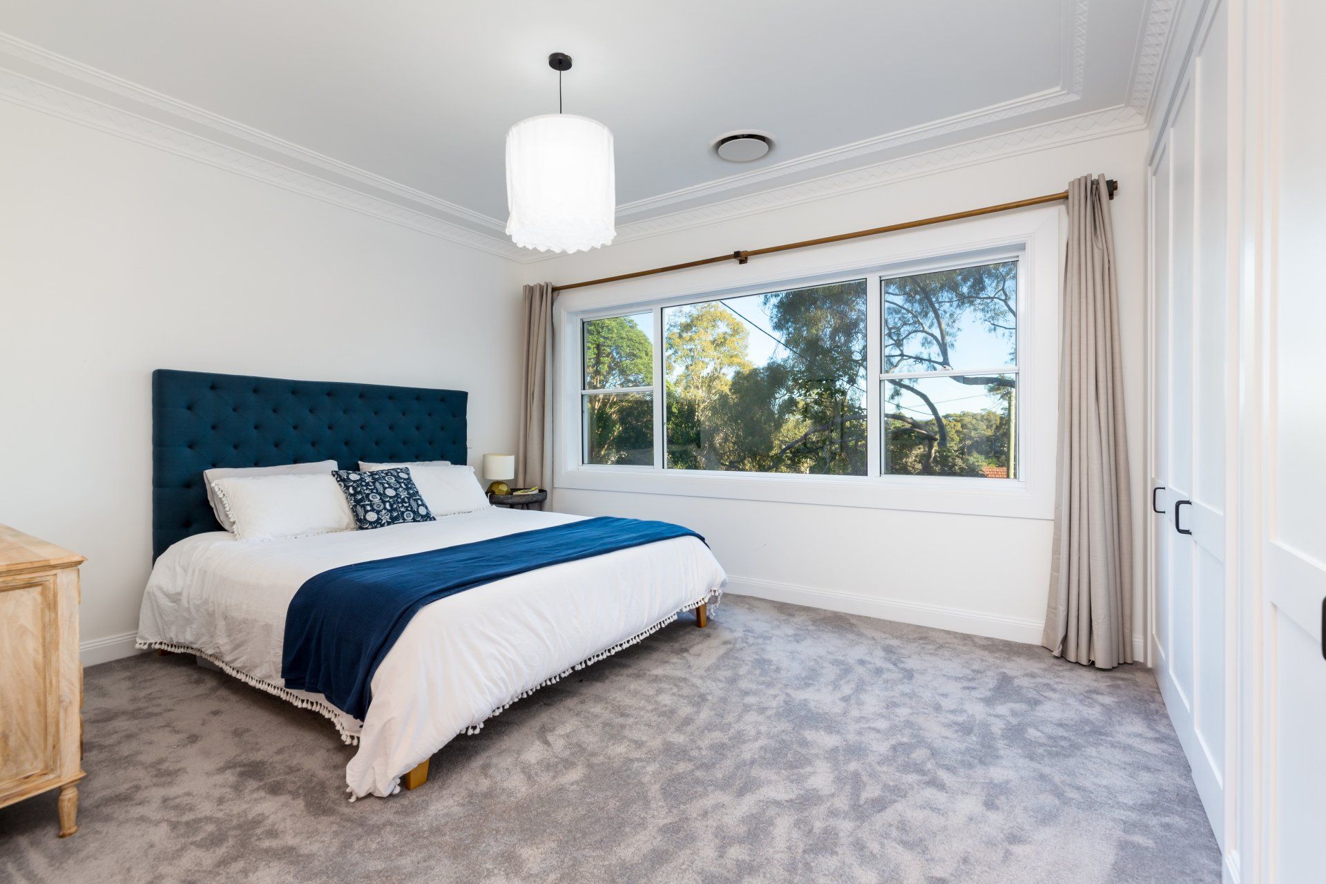 Bedroom with blue tufted headboard, white bedding, large window, and gray carpet.