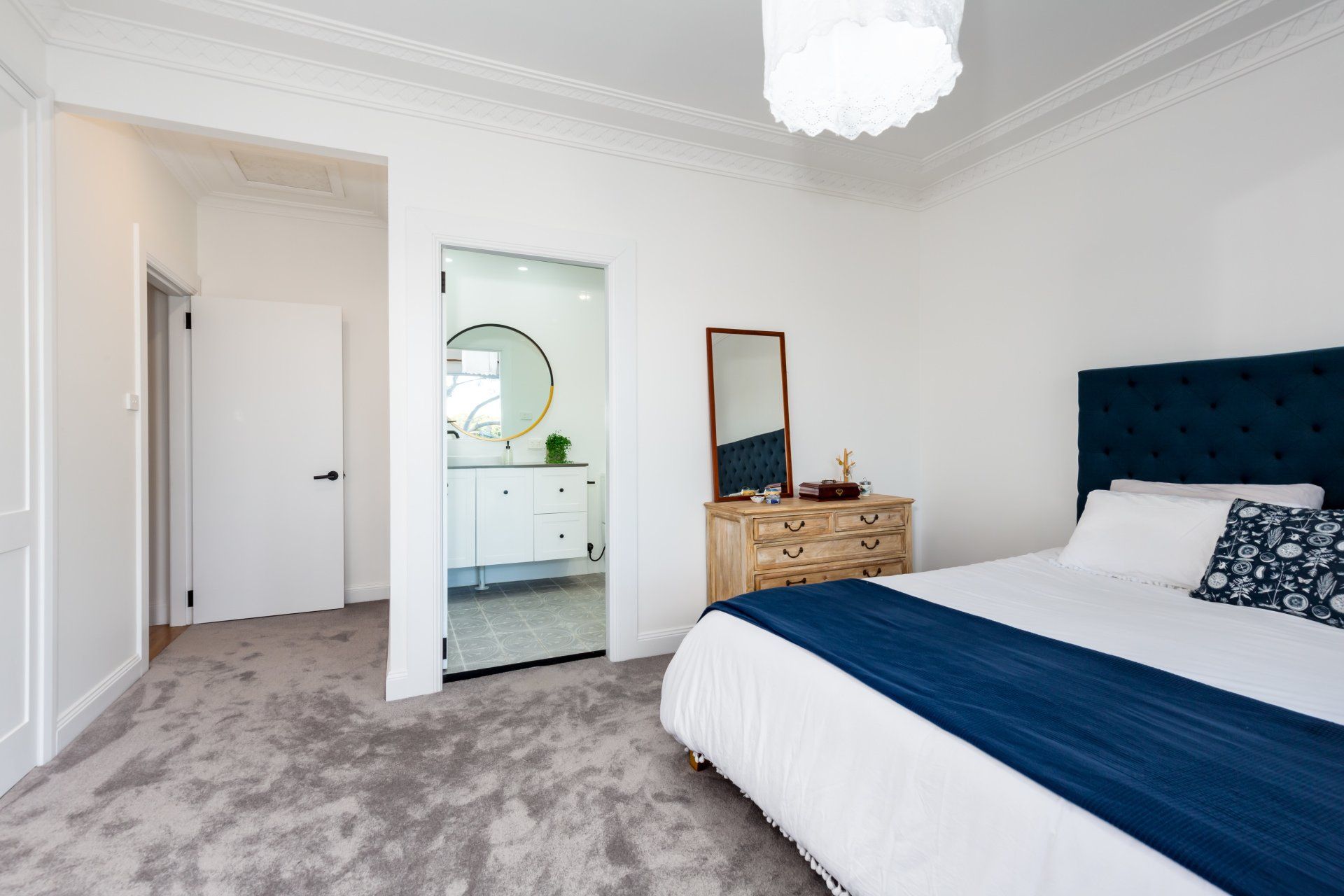 Bedroom with a blue bed, dresser, and a doorway to a bathroom with a round mirror.