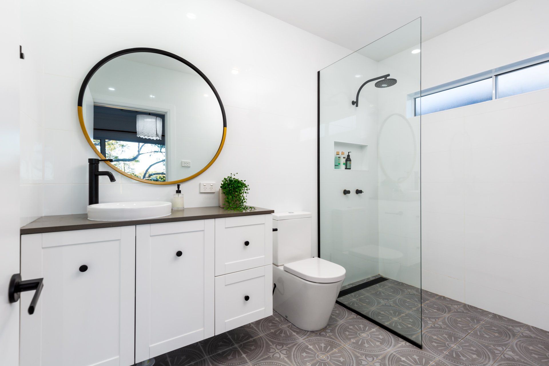 Modern white bathroom with black accents, a round mirror, and a glass shower.