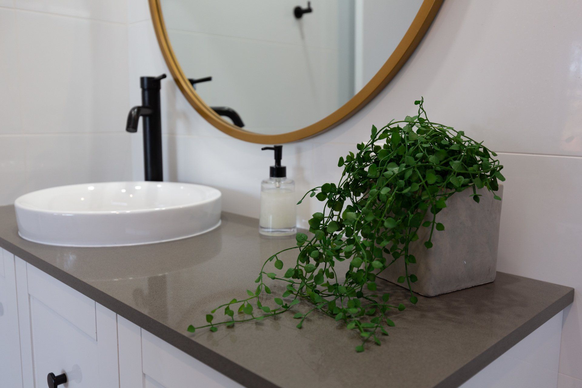 Bathroom countertop with a round sink, gold mirror, black faucet, and a potted trailing plant.