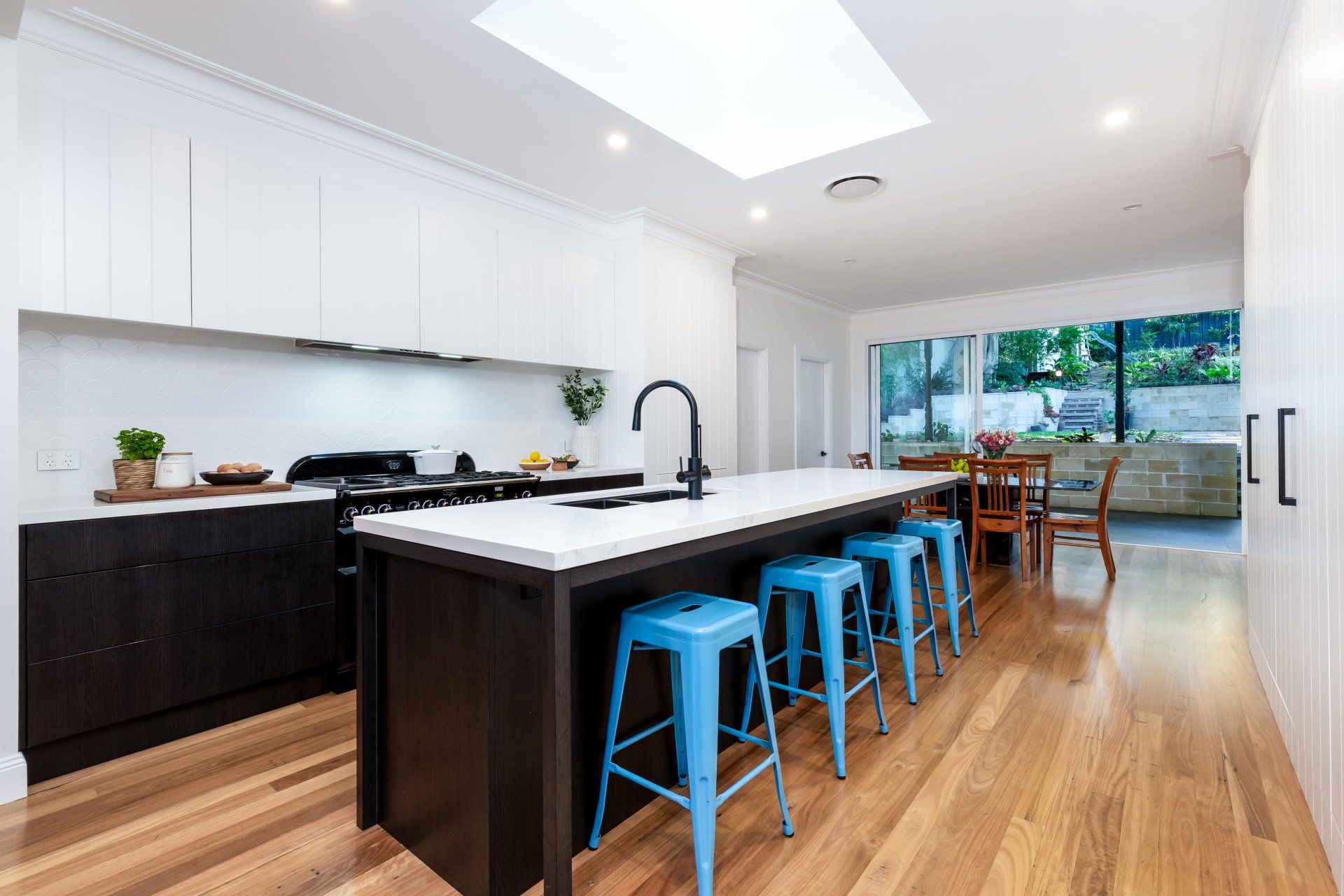 Modern kitchen with dark and white cabinets, large island with blue stools, and skylight.