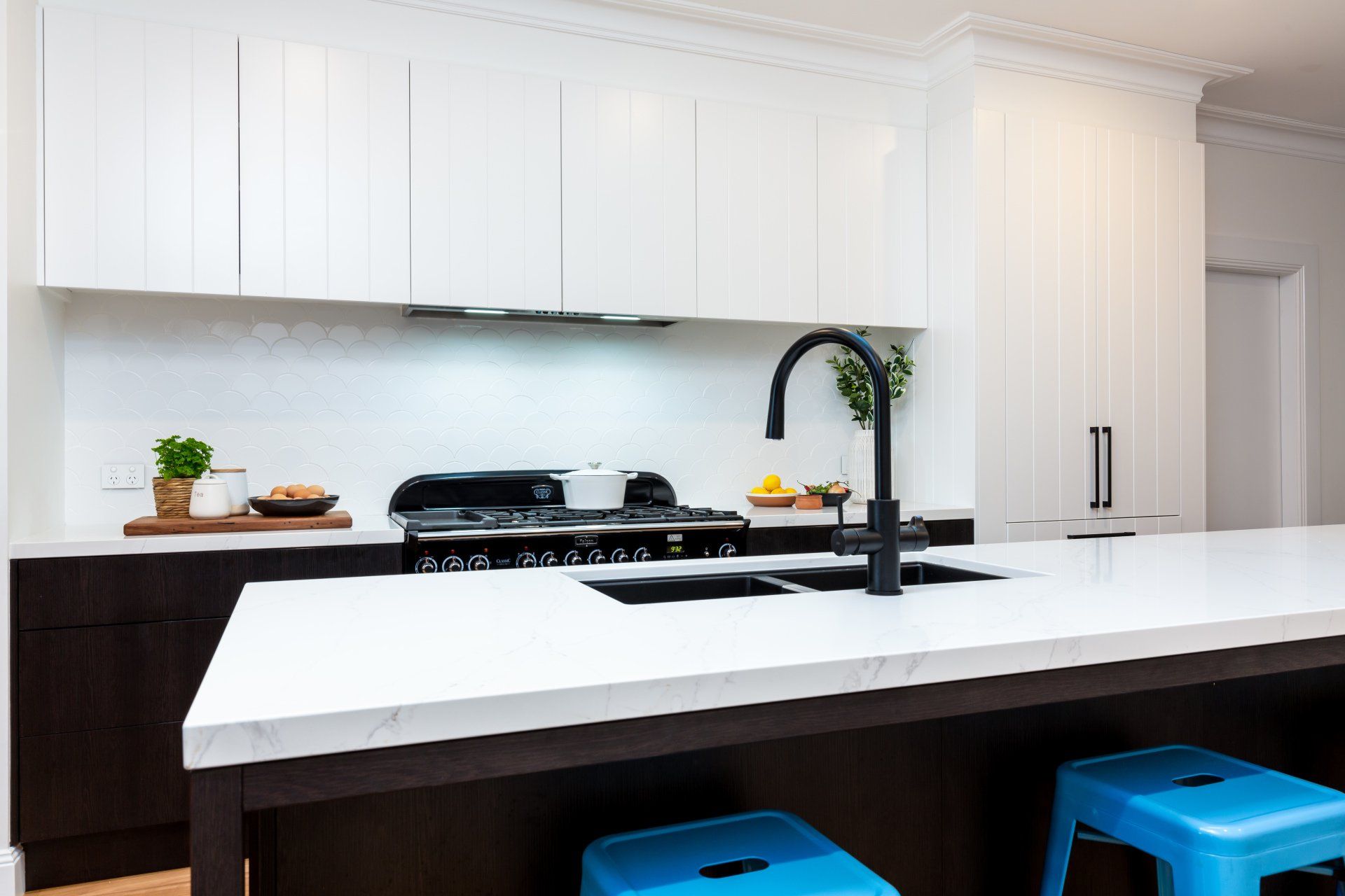 Modern white kitchen with black accents, island with blue stools.