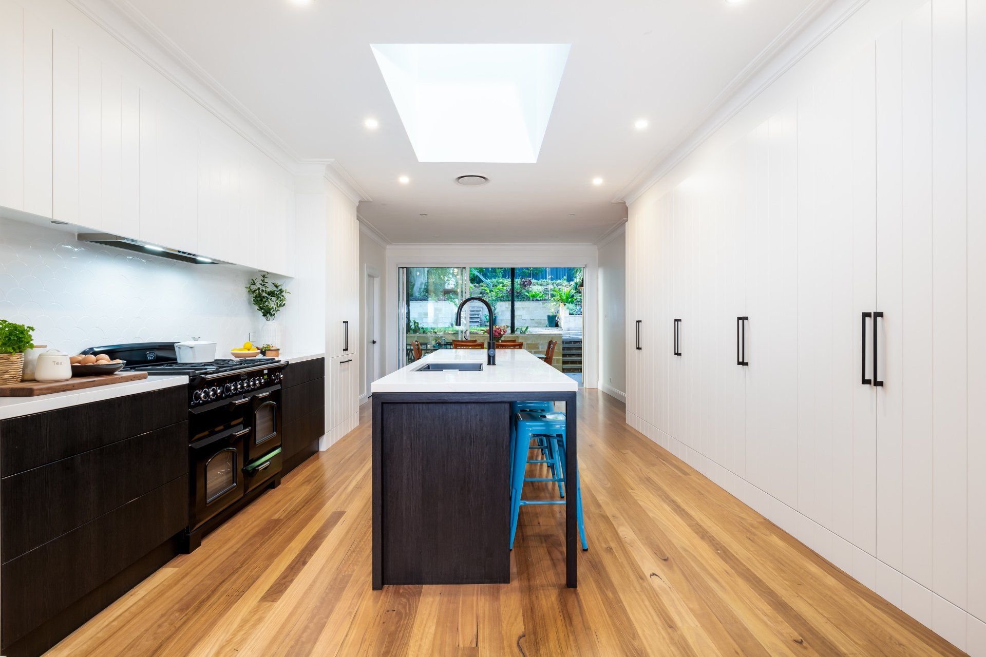 Modern kitchen with white cabinets, dark island, blue stools, and hardwood floors.