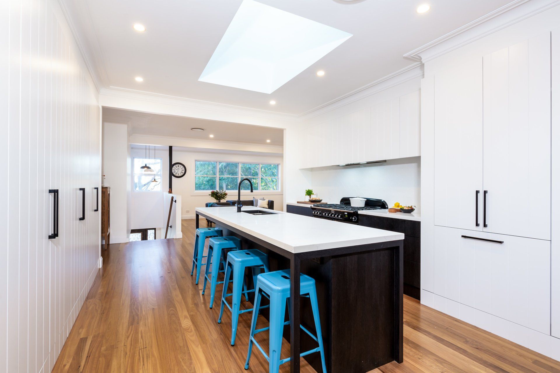 Modern kitchen with white cabinets, wooden floors, and a dark island with blue stools.