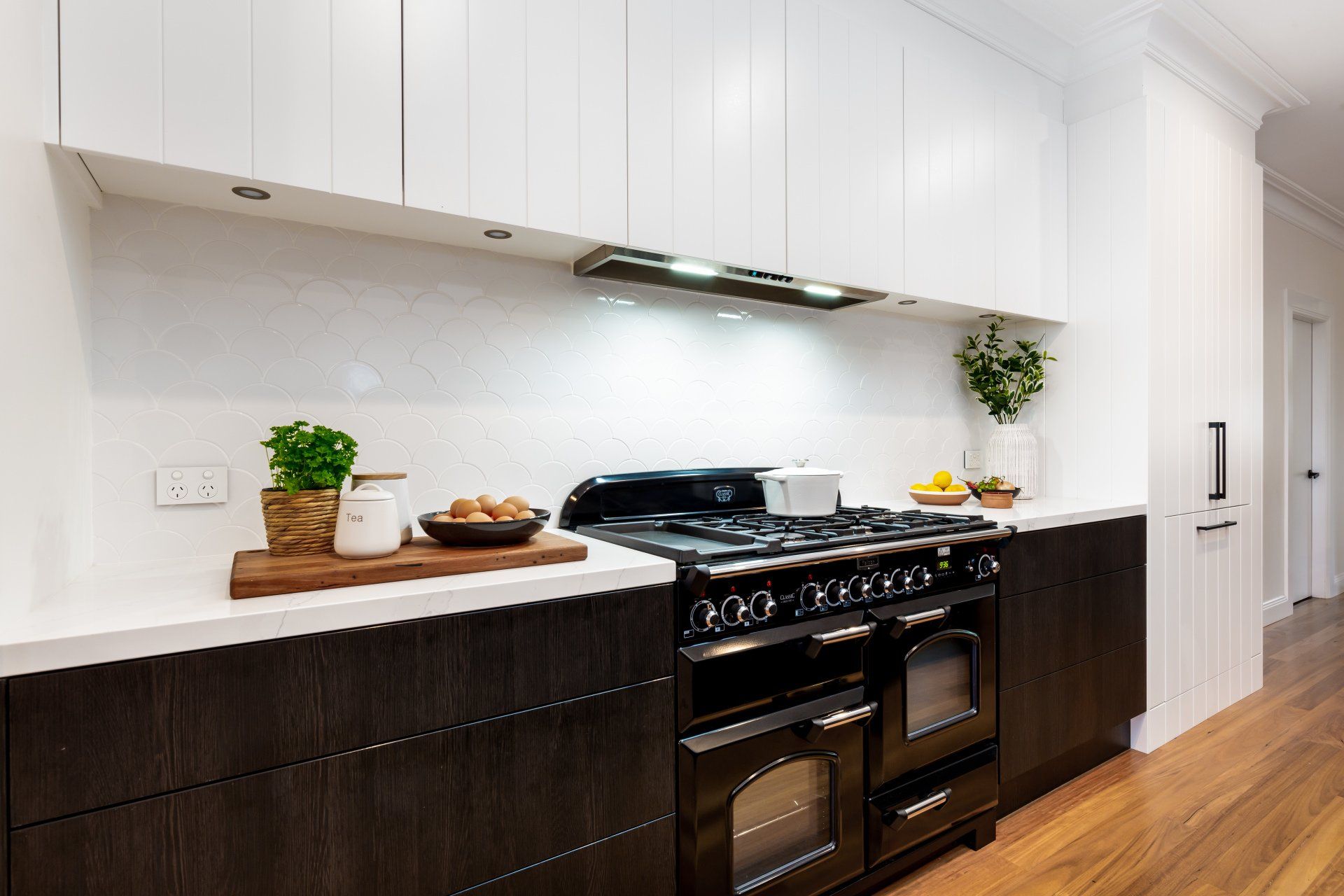 Kitchen with dark cabinets, black stove, white countertops, and white upper cabinets.