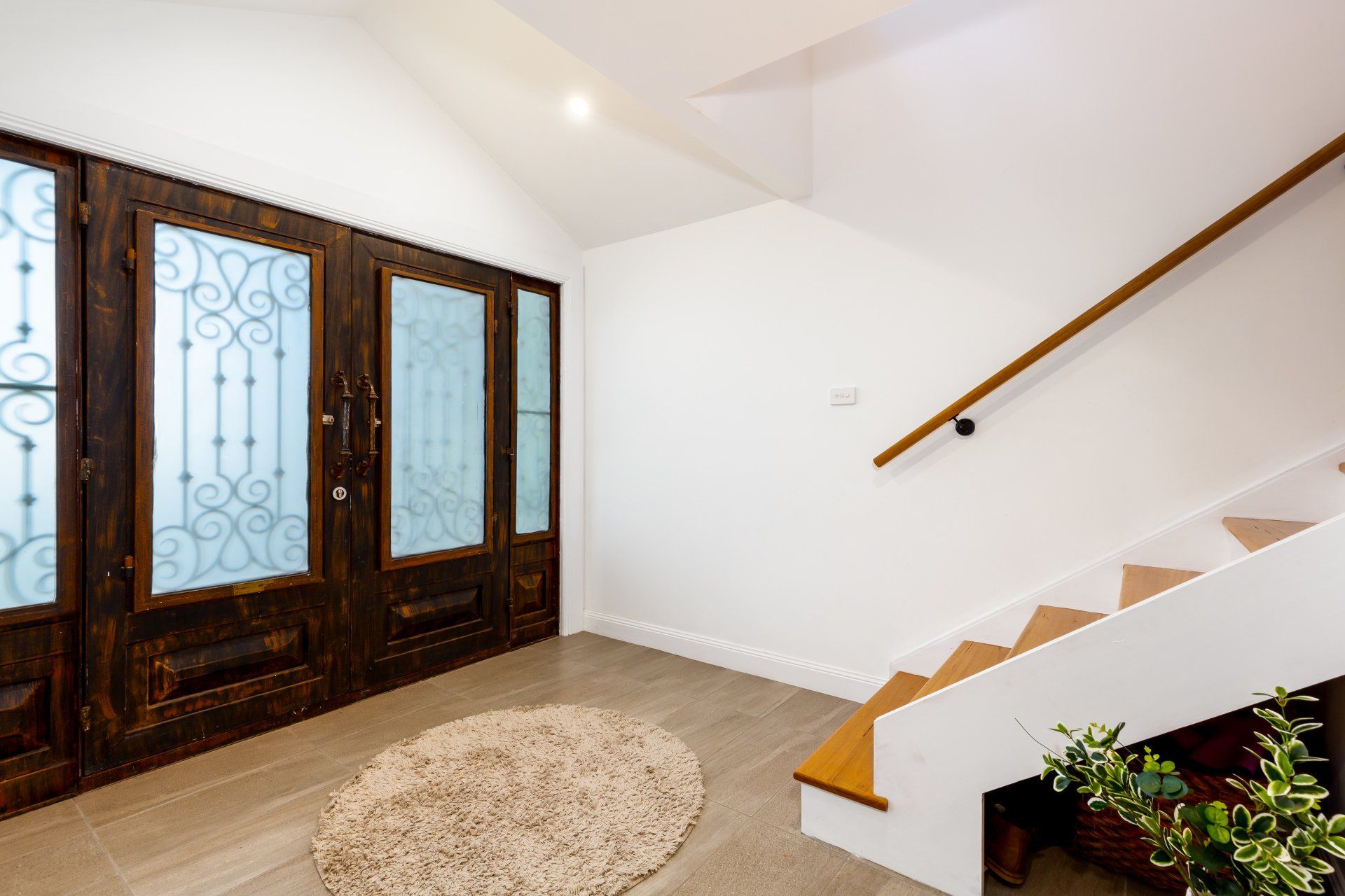 A wooden door with decorative glass next to a white staircase. A round rug on the floor.