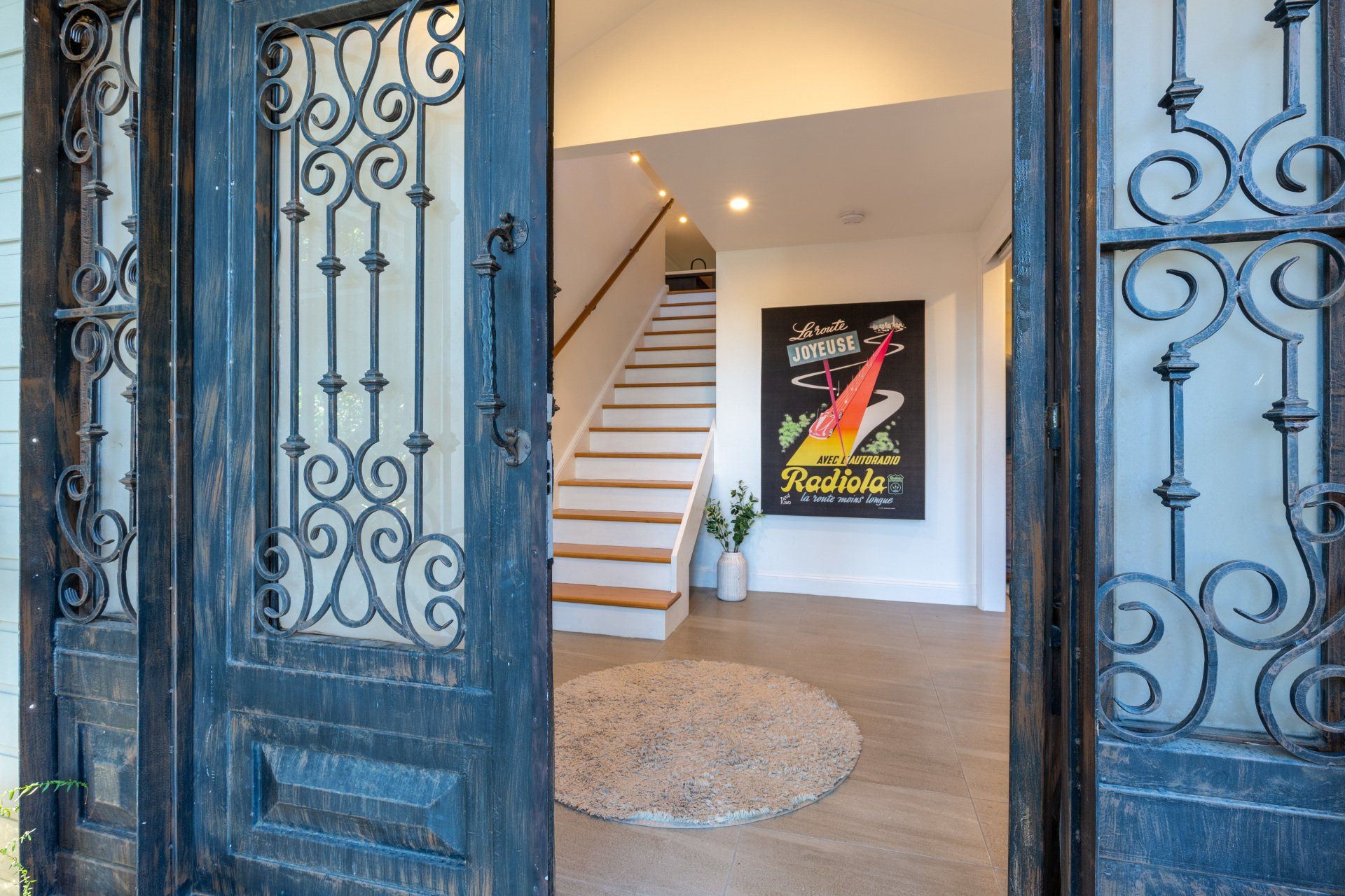 Ornate black doors open to a light-filled entryway with a staircase and art.