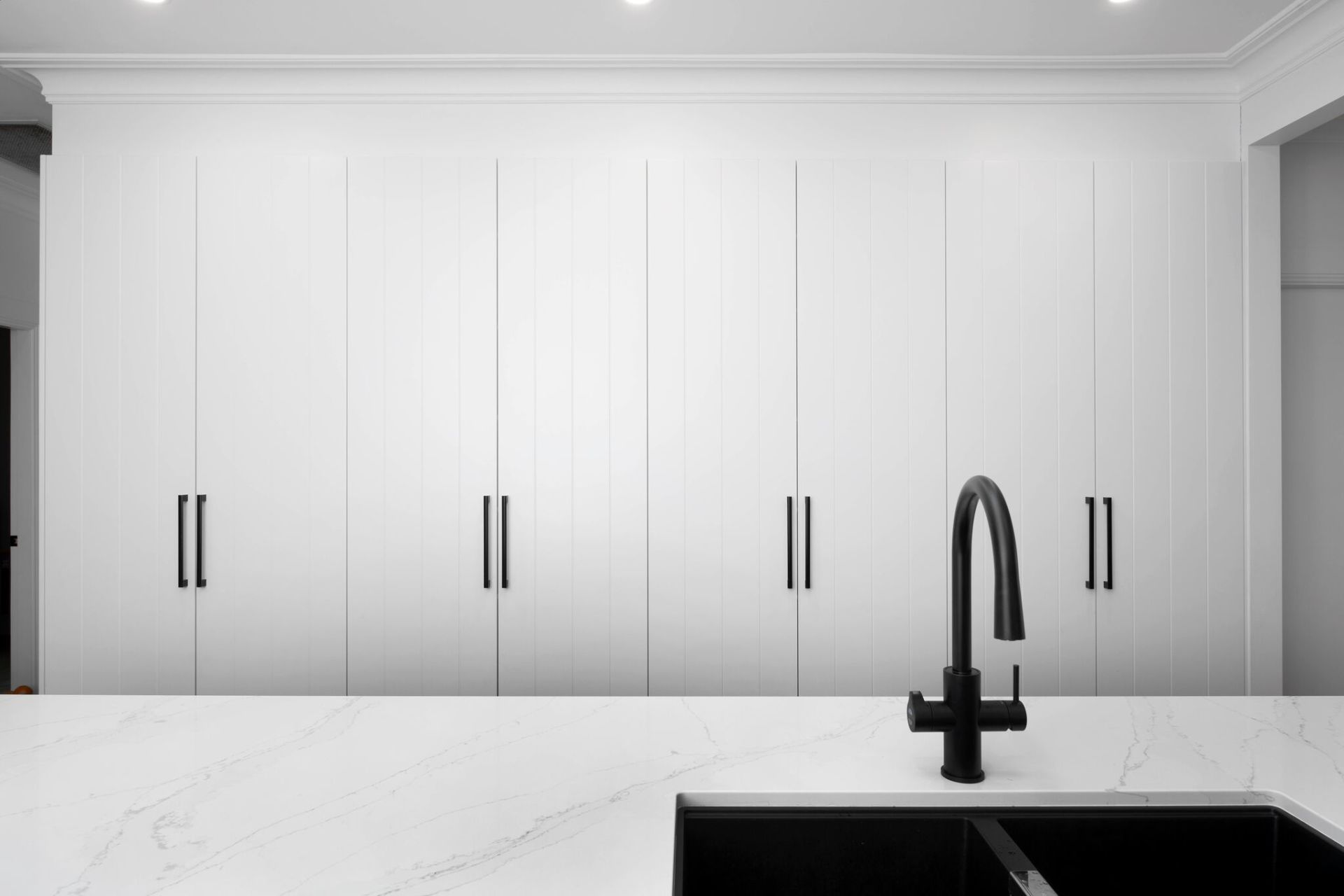 White kitchen cabinets with black hardware, countertop, and faucet.