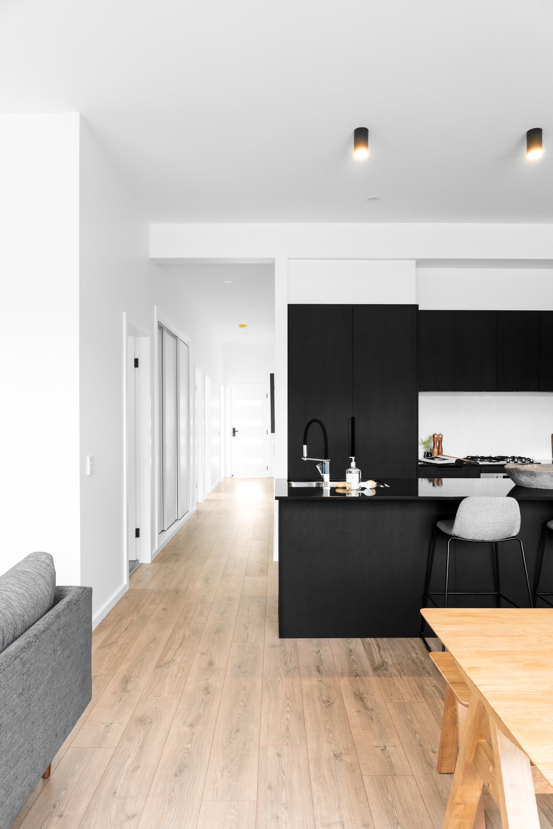 Modern kitchen with black cabinets, light wood floor, and hallway.