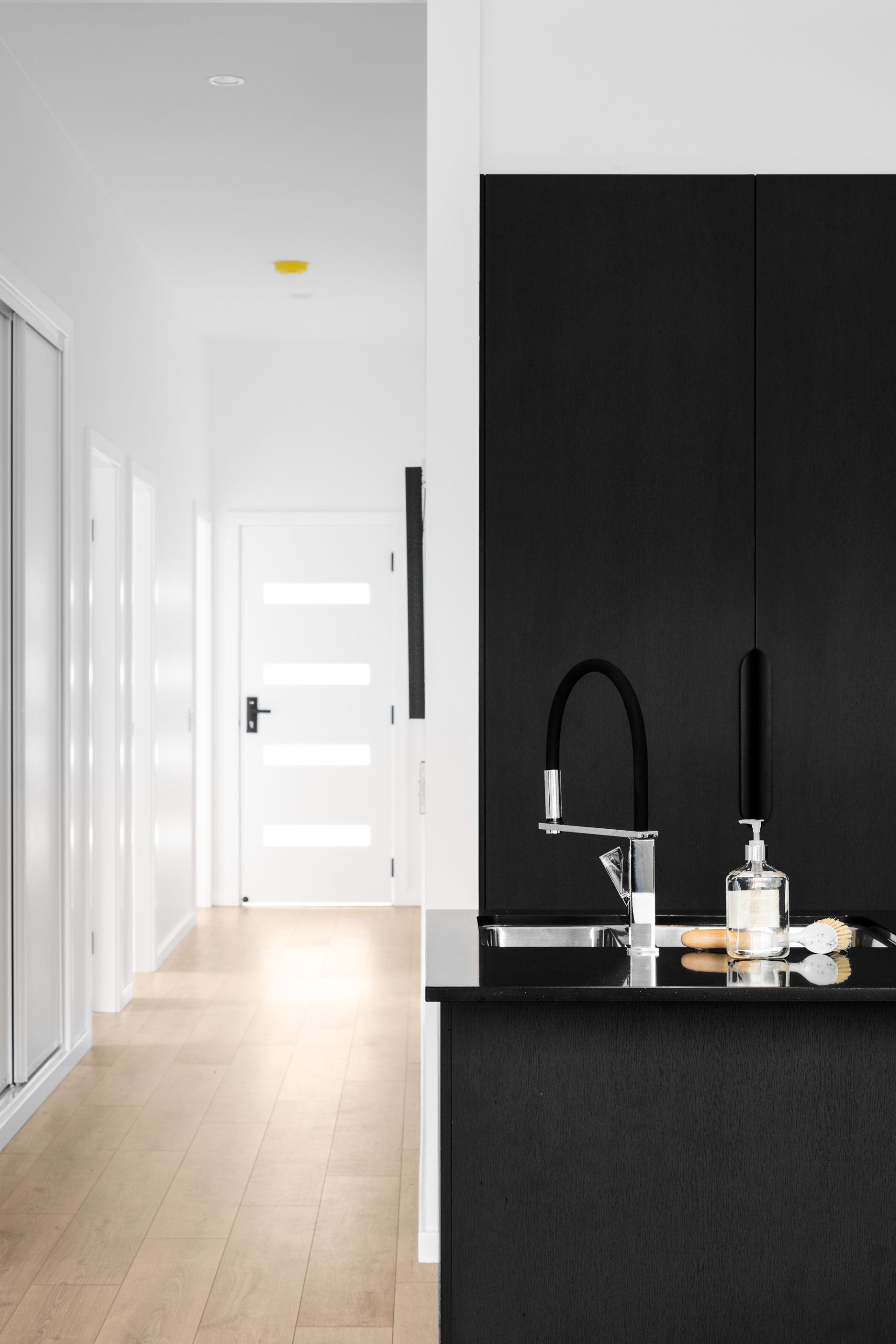 Modern kitchen with black cabinets, stainless steel faucet, and a hallway leading to a white door.