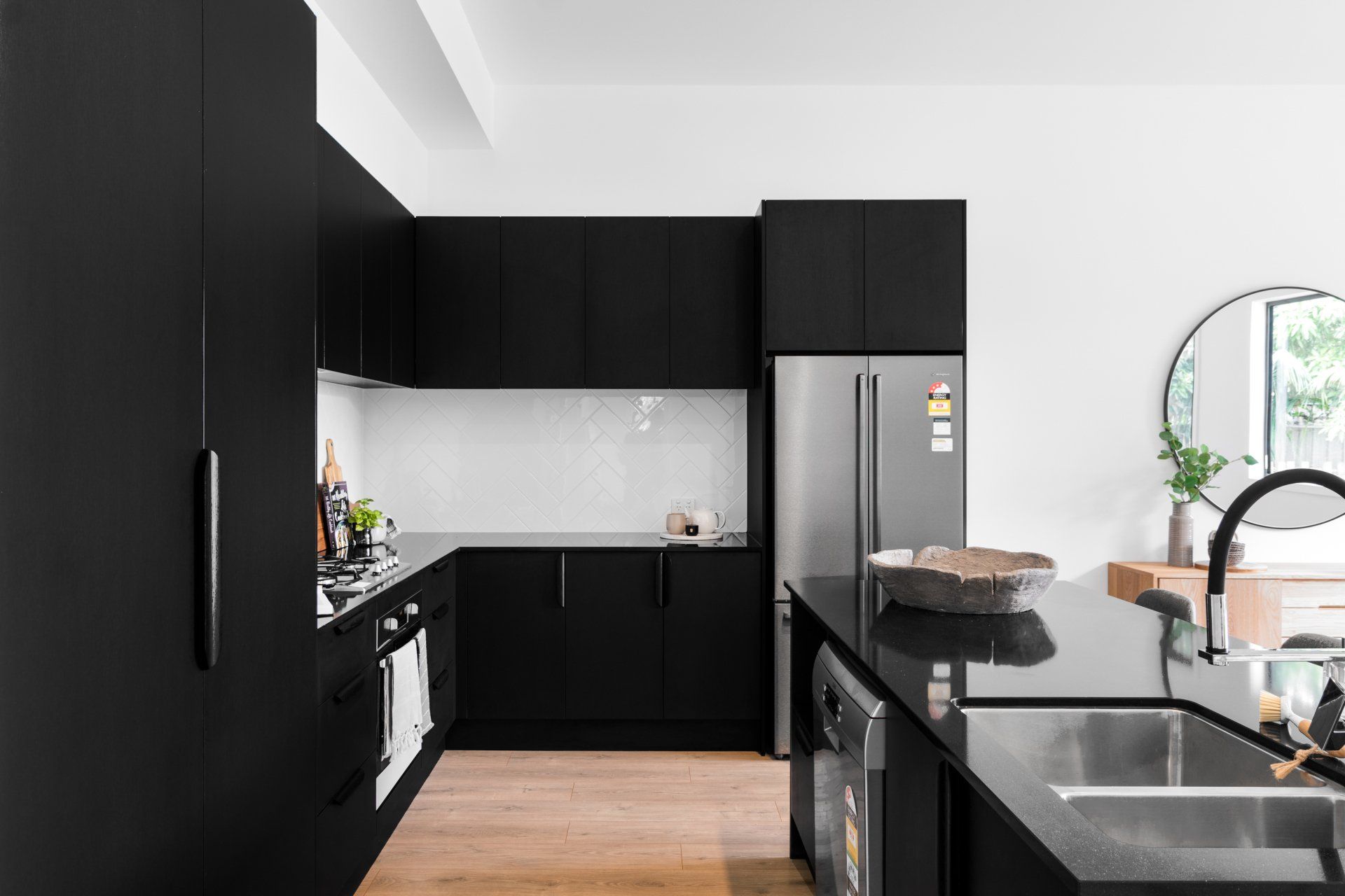 Modern black kitchen with stainless steel fridge, island, and white backsplash.