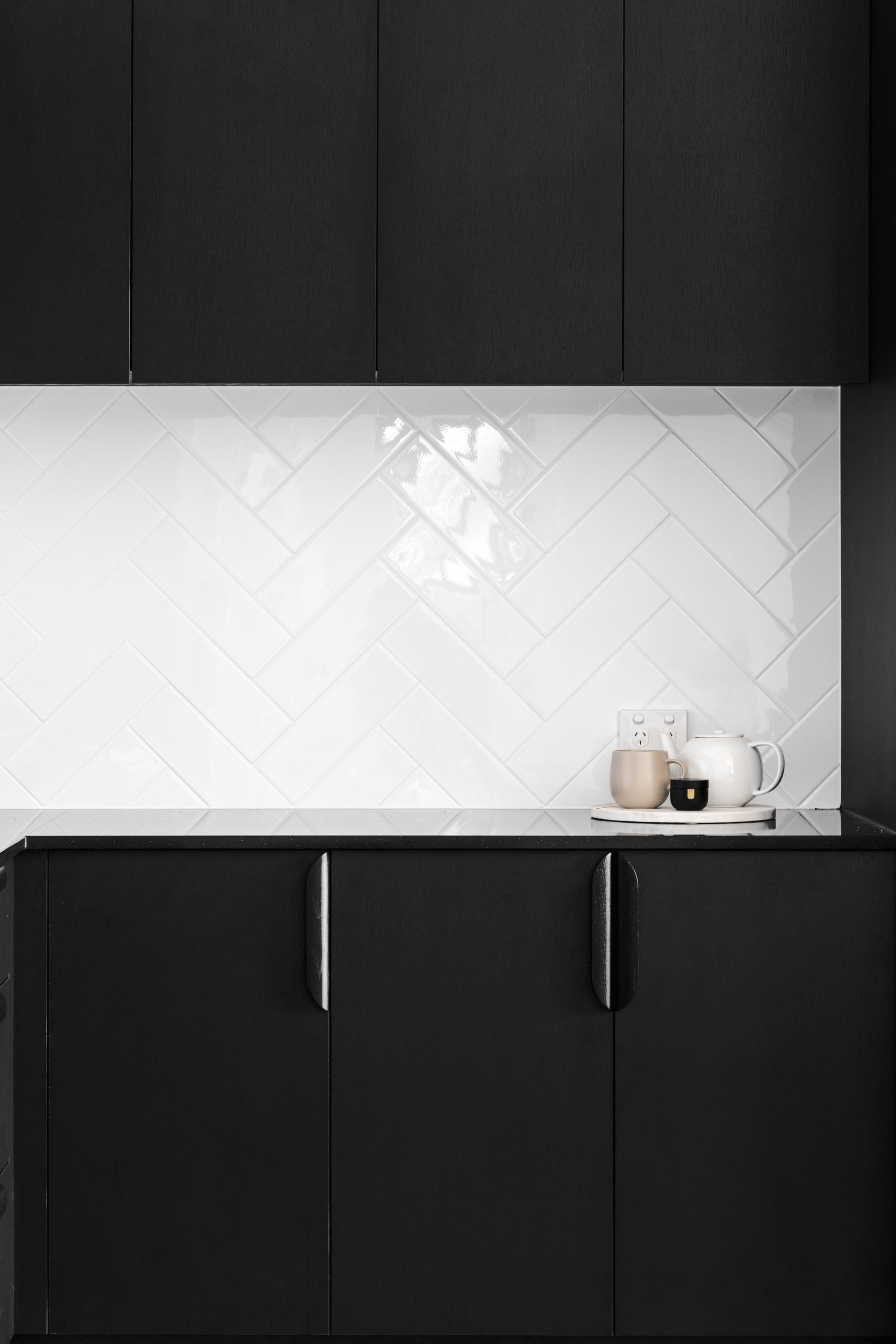 Black and white modern kitchen with herringbone backsplash, black cabinets, and countertop.