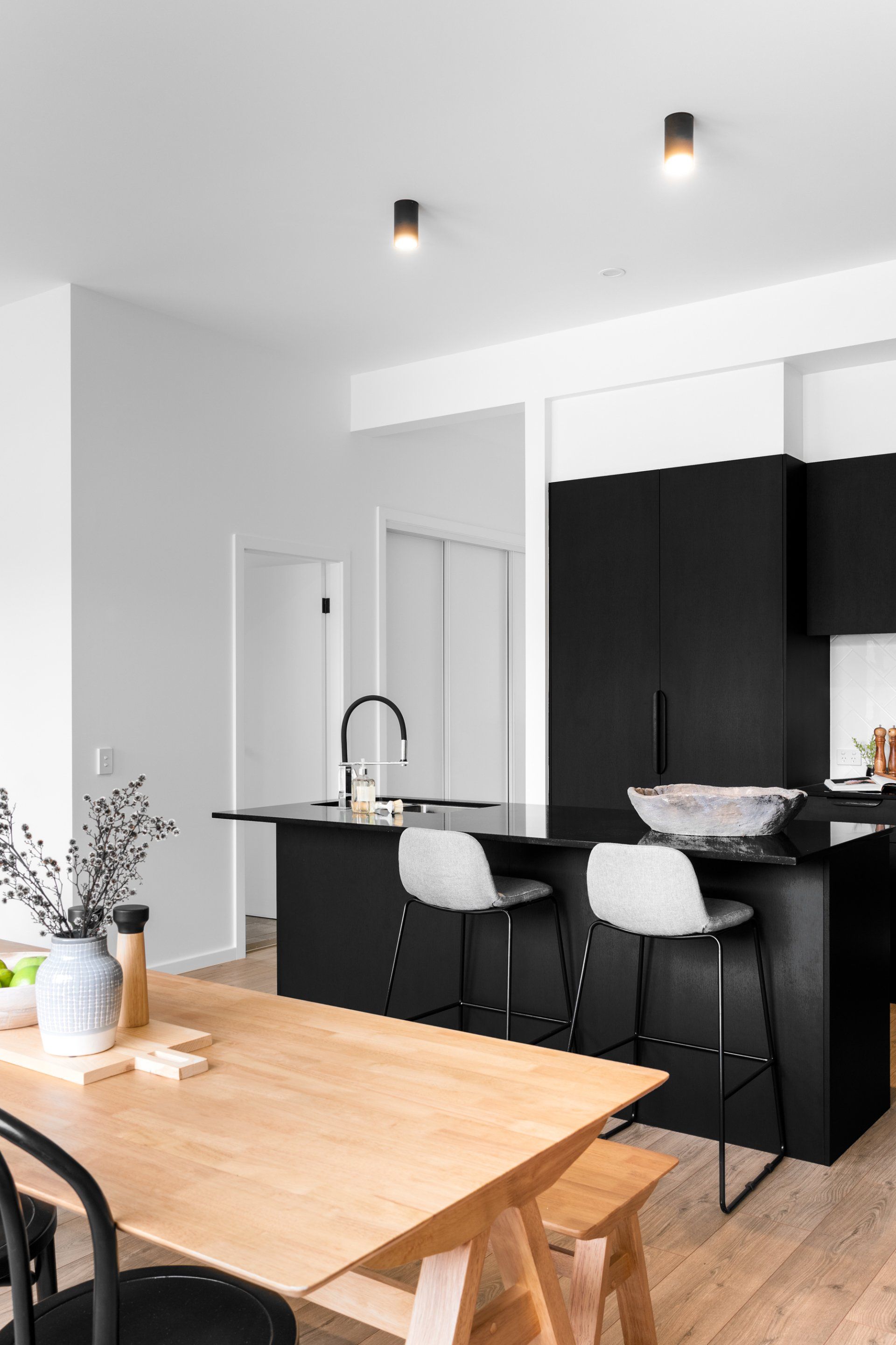 Modern kitchen with black island, light wood table, and white walls.