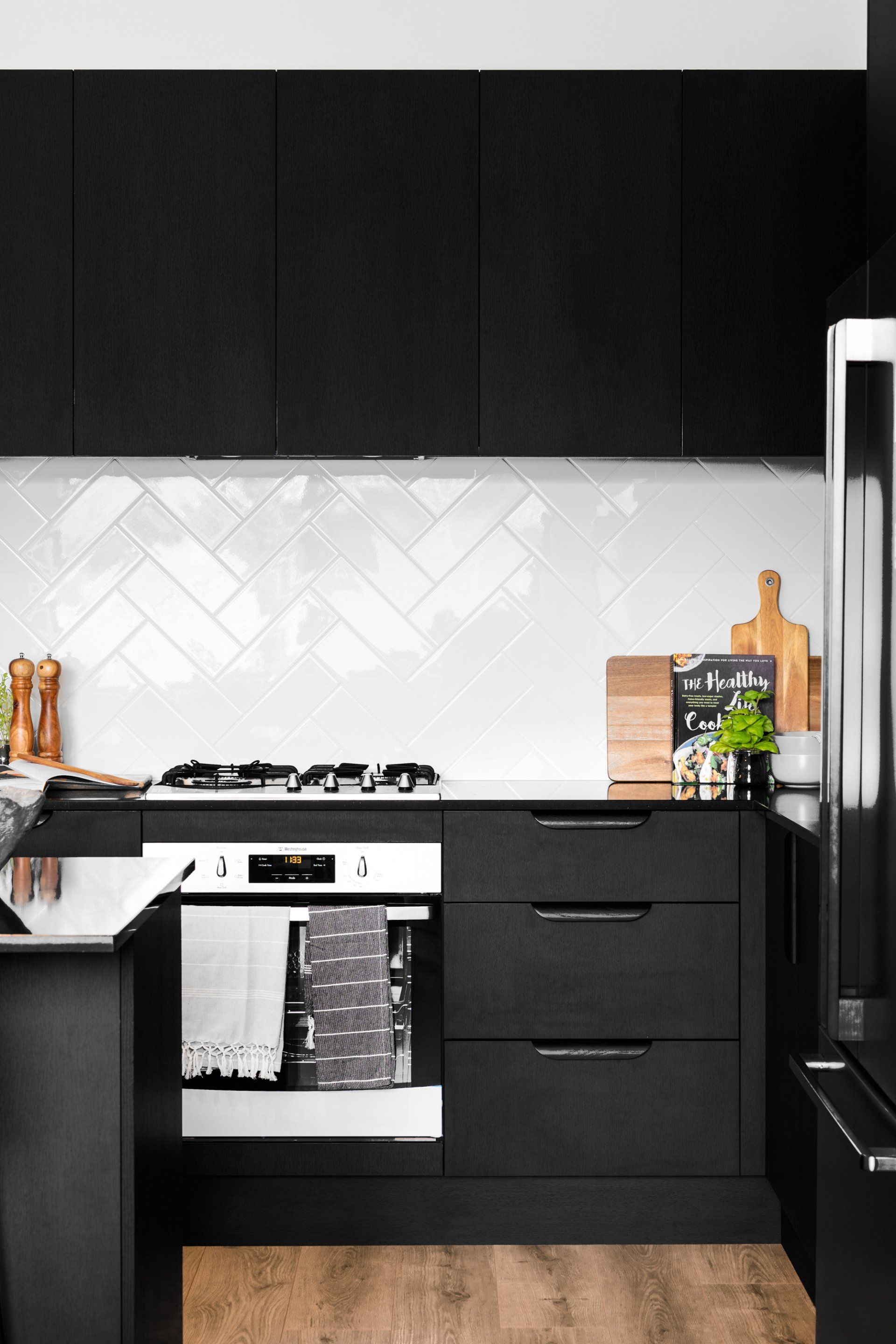 Black and white kitchen with black cabinets, herringbone tile backsplash, and wooden countertops.