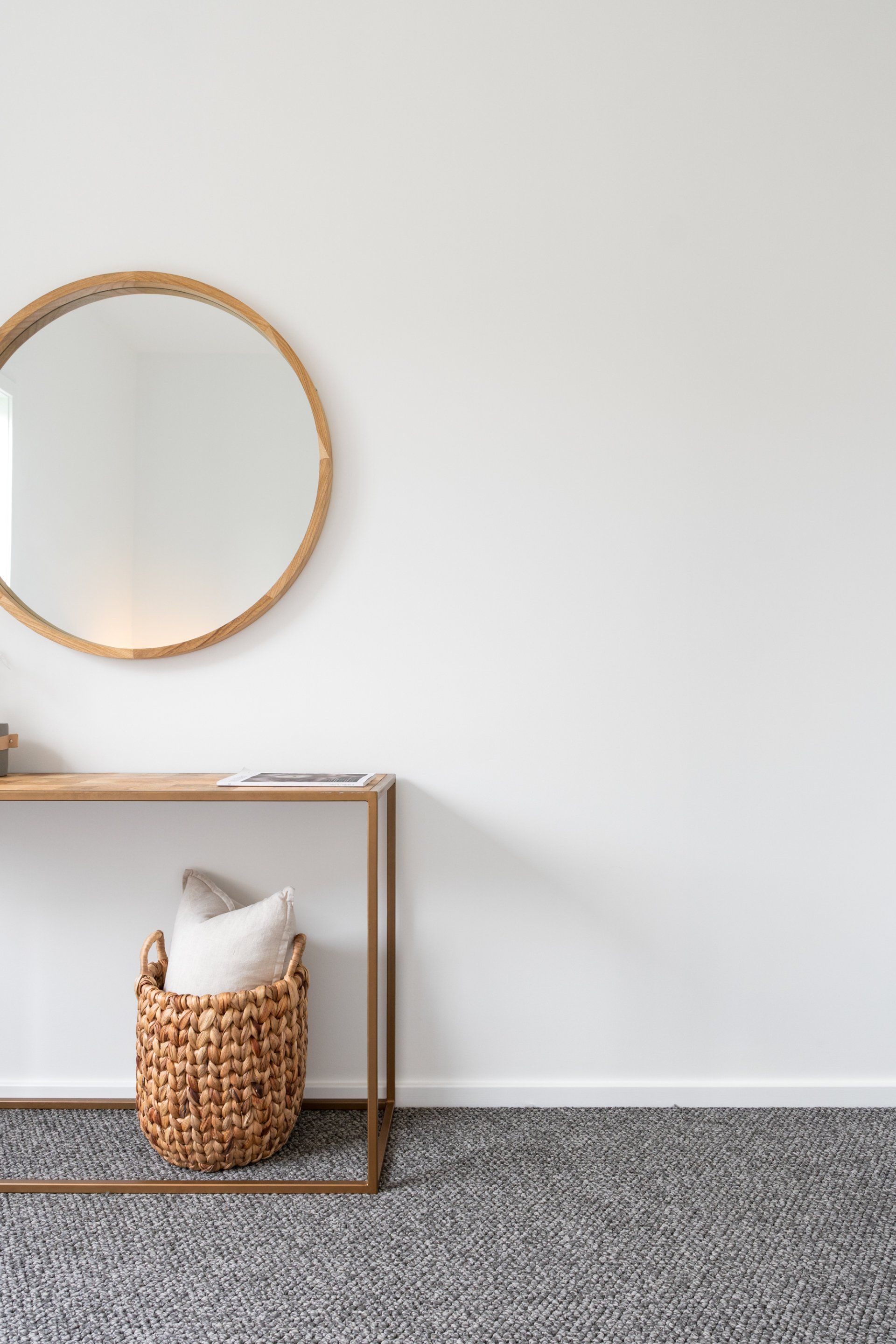 Round mirror with woven frame over a console table with a basket and pillow on a patterned rug.