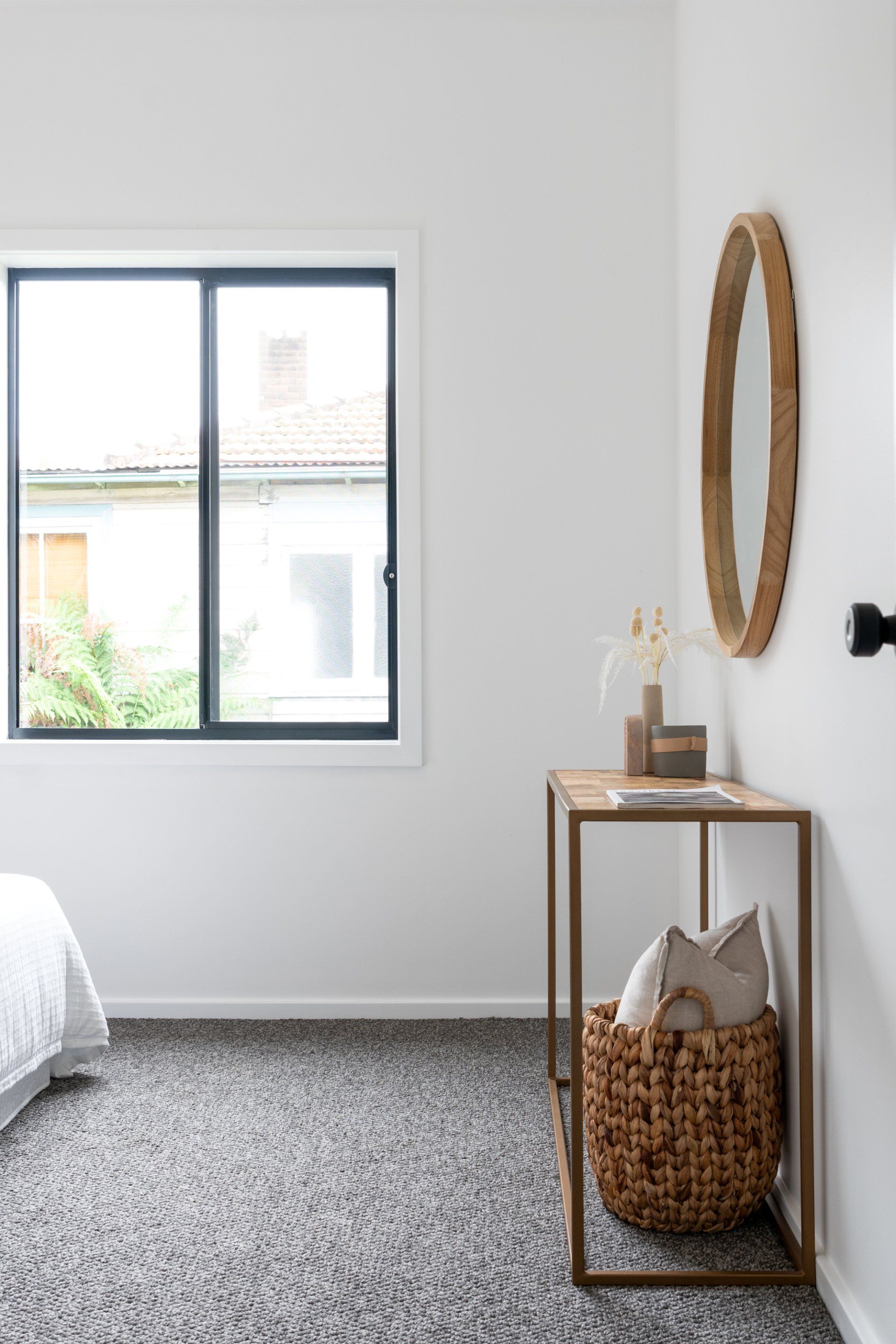 Bedroom with window, table, mirror, and woven basket. White walls, gray carpet.