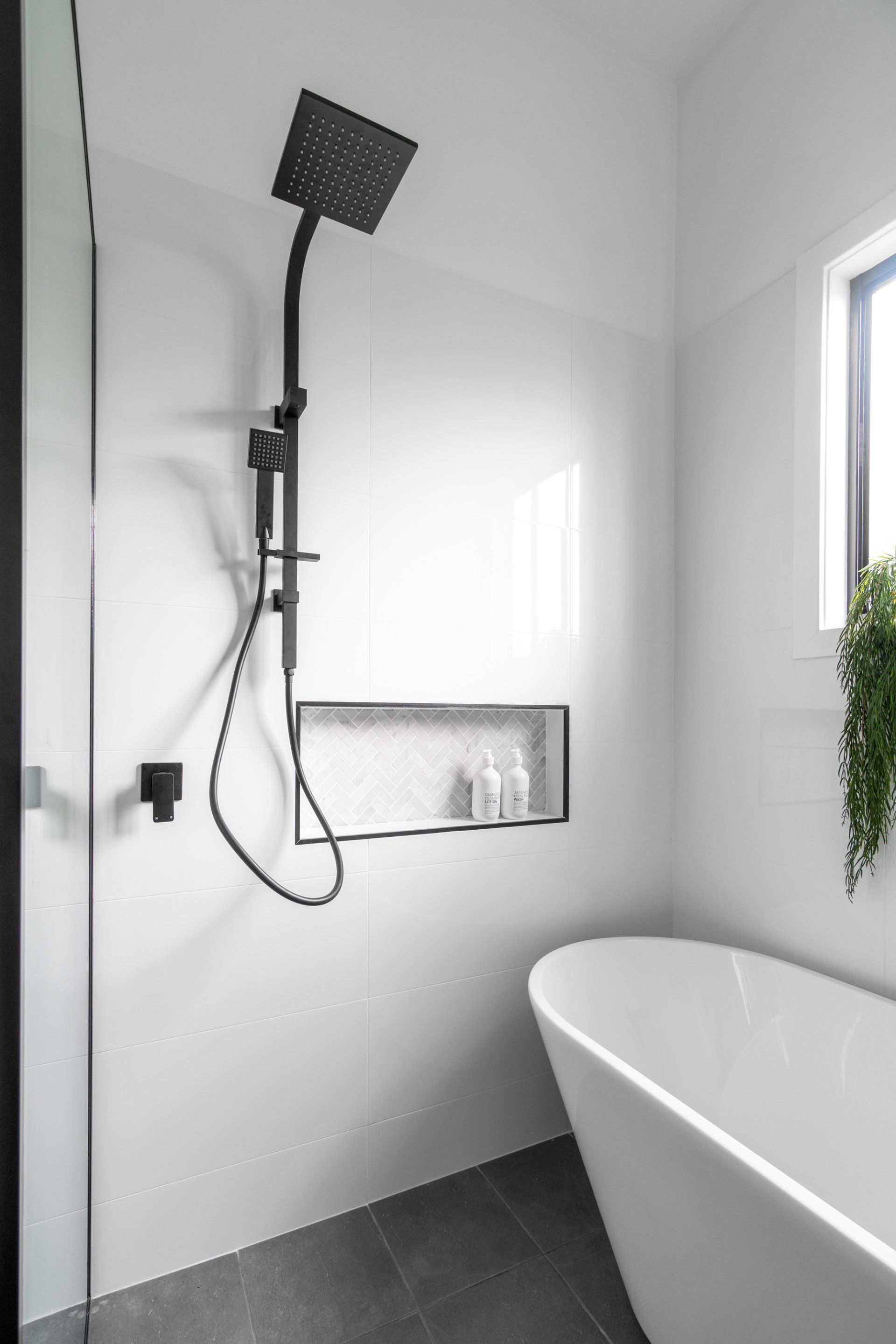 Black showerhead, white bathroom with built-in shelf, tub, and glass door.
