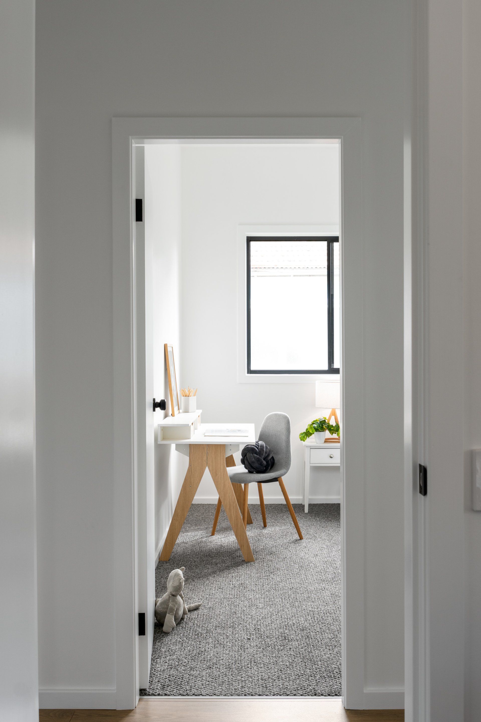 Doorway view of a white office with a desk, chair, window, and patterned carpet.