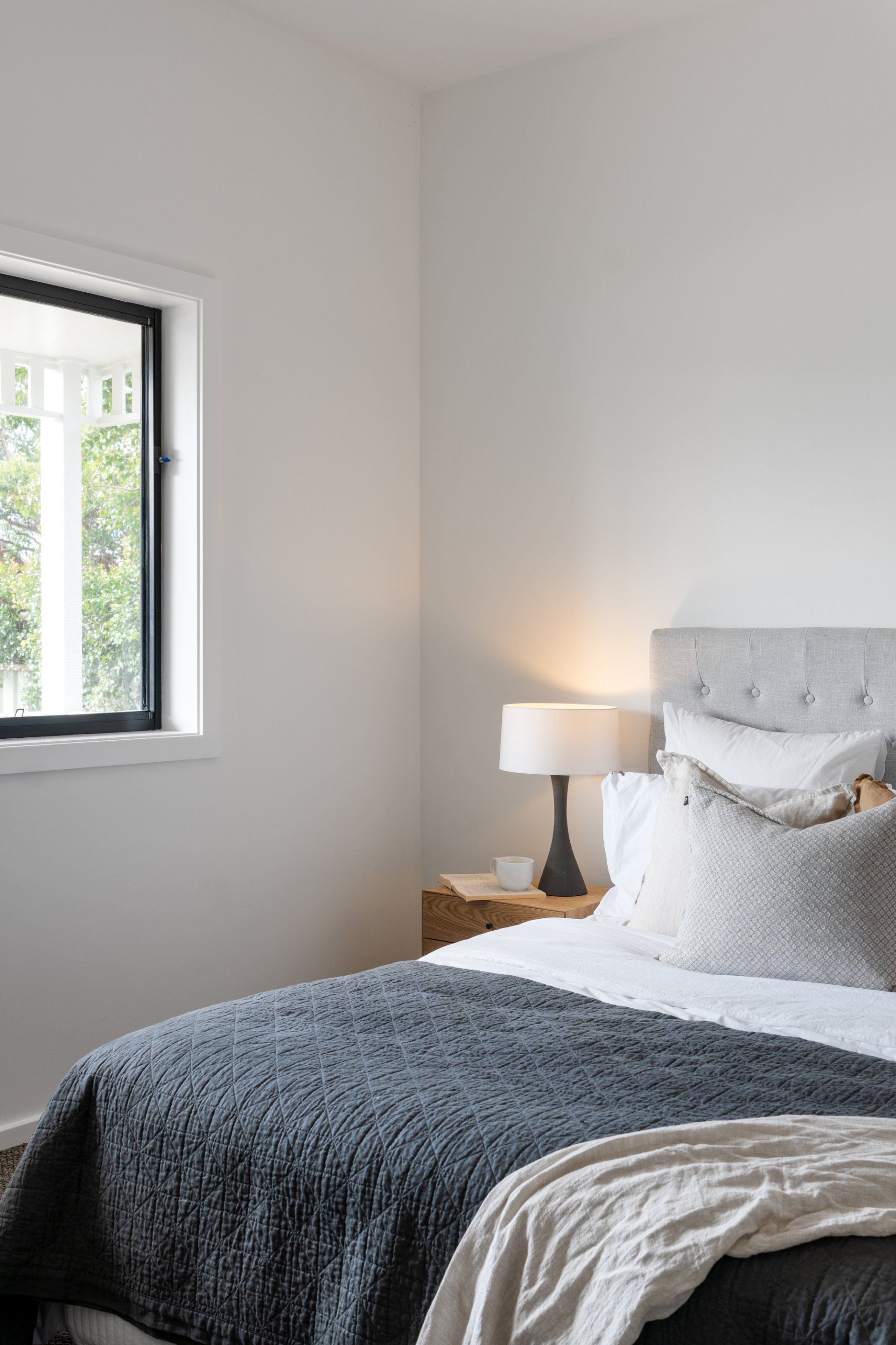 Bedroom with bed, nightstand, lamp, window with a view, and white walls.