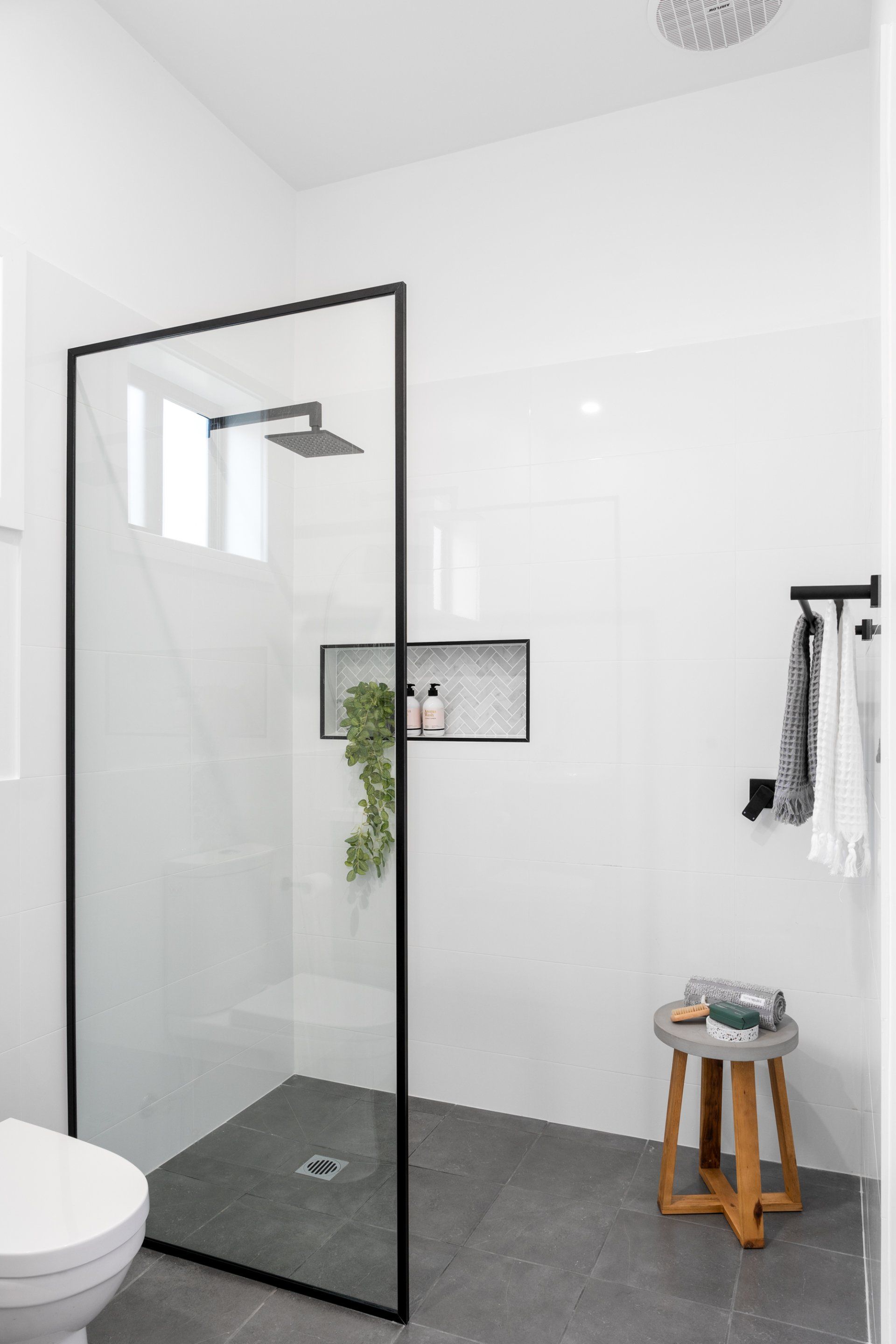 Modern bathroom with a glass shower enclosure, white walls, and a gray tiled floor.