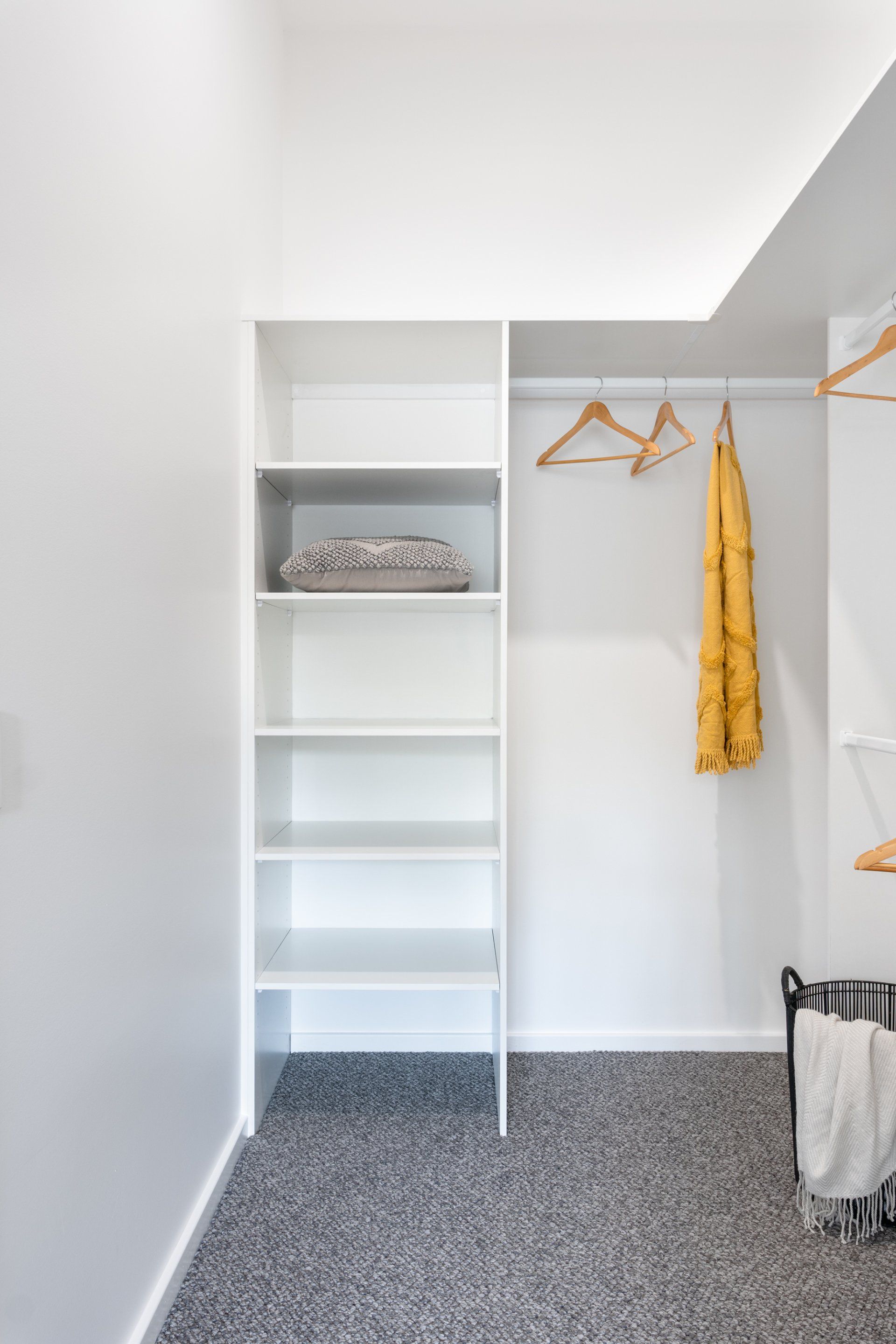 White closet with shelves and hanging rod; folded clothes on shelves, yellow dress hanging.