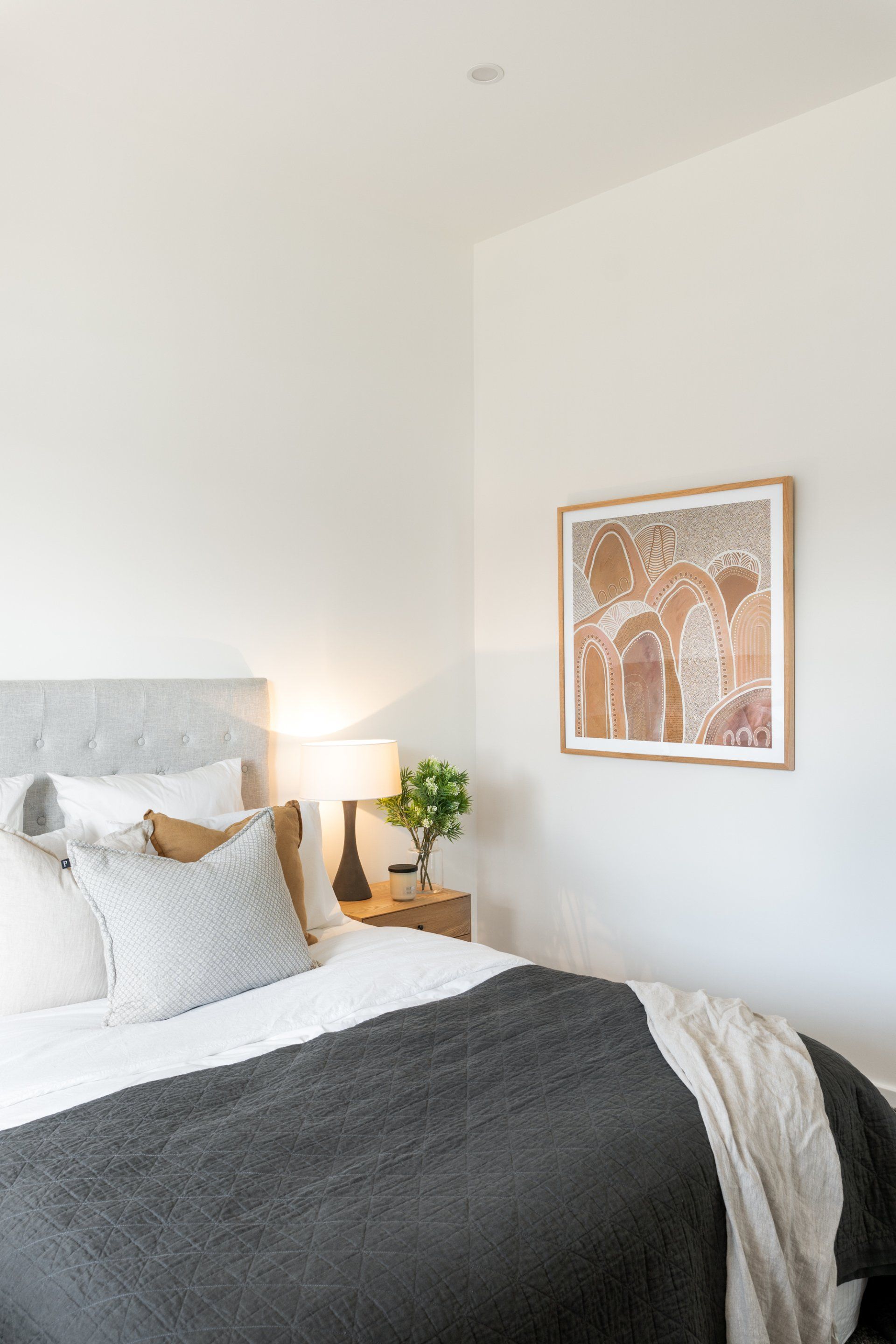 Bedroom with a bed, lamp, artwork, and a nightstand. Gray and white bedding.