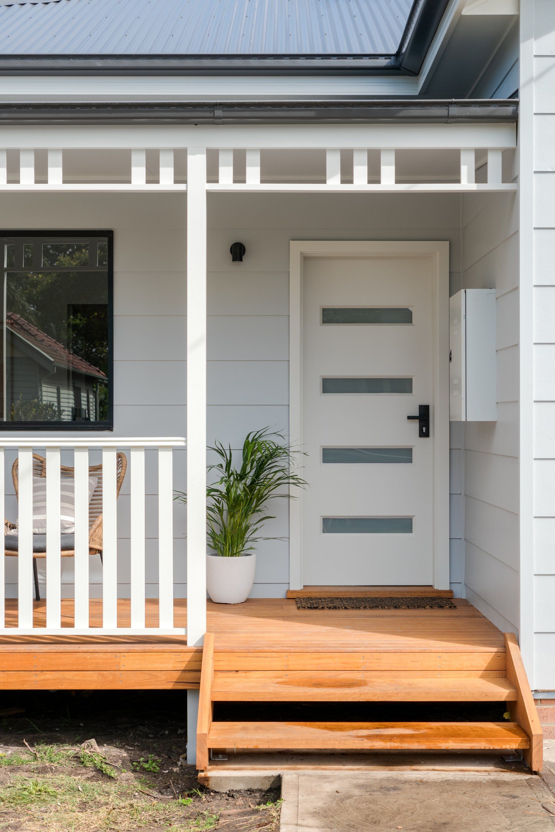White house entrance with wooden porch and steps, white door with horizontal glass panels.