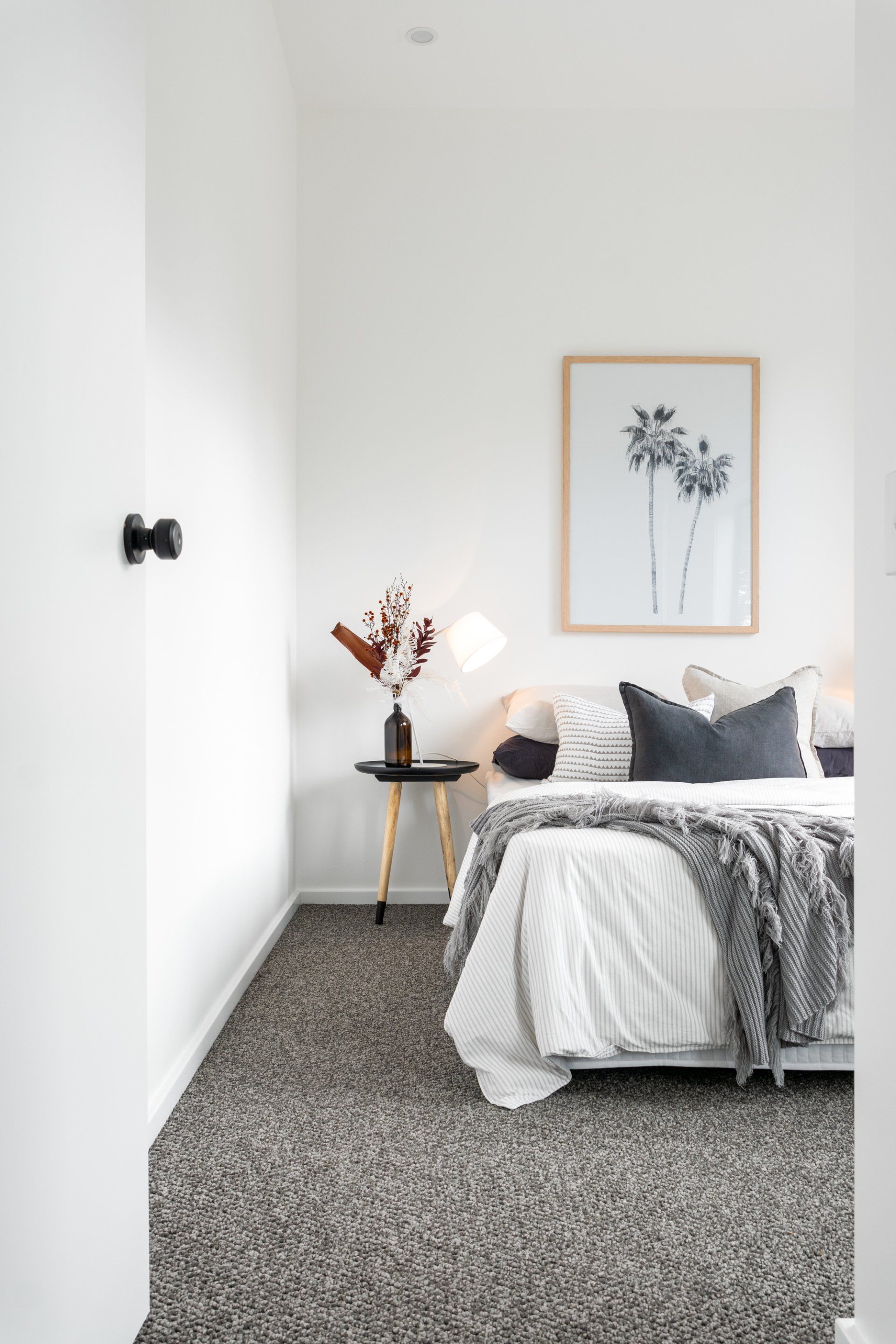 Bedroom with white walls, gray patterned carpet, bed with gray and white bedding, and artwork.