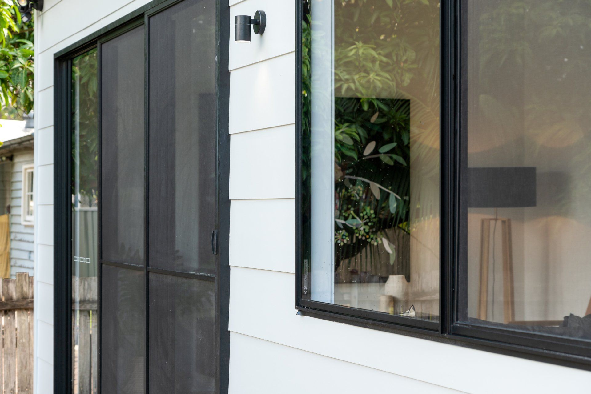 Exterior view of a white building with black-framed sliding doors and windows. Interior reflected in the window.