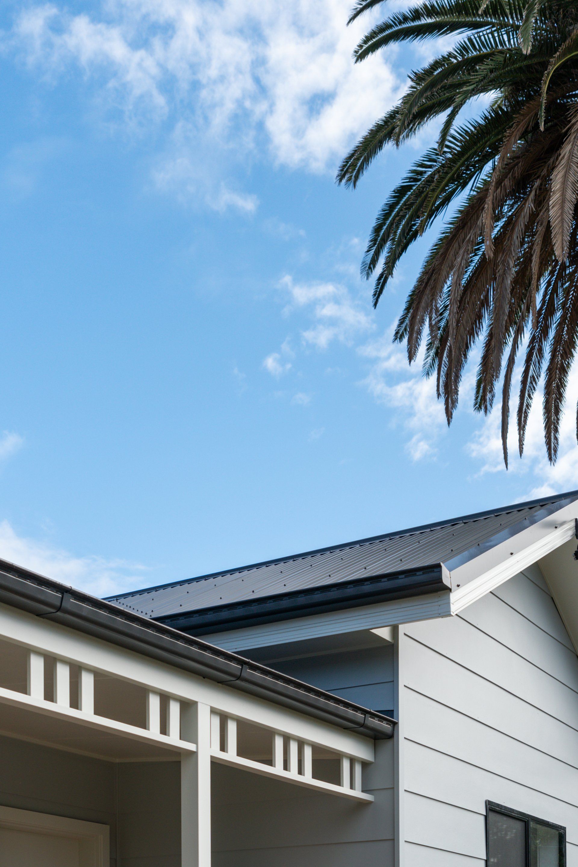 White house with dark roof, palm tree, and blue sky.