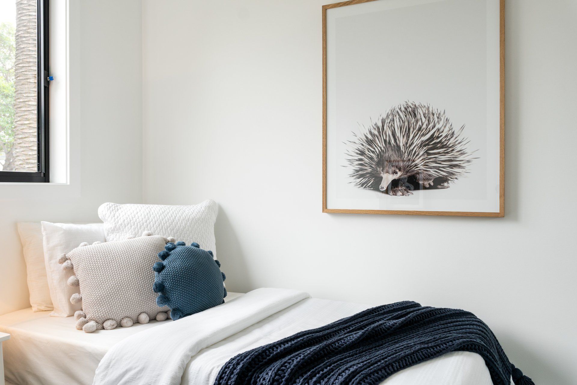 Bedroom with white walls, a bed with pillows and a blanket, and a hedgehog art print.