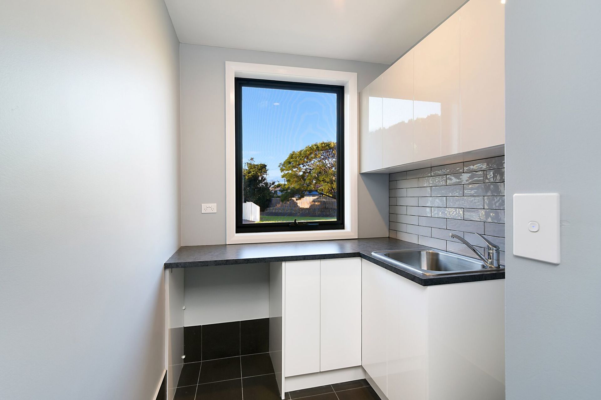 Small white kitchen with a window looking outside; black countertop and backsplash.