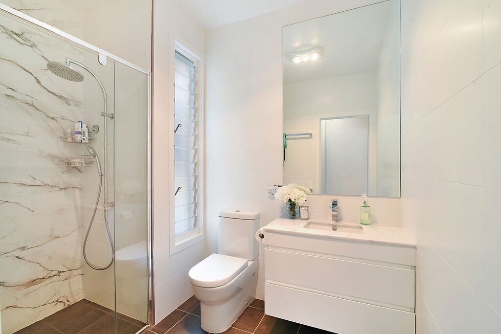 White bathroom with a glass shower, toilet, sink, and mirror.