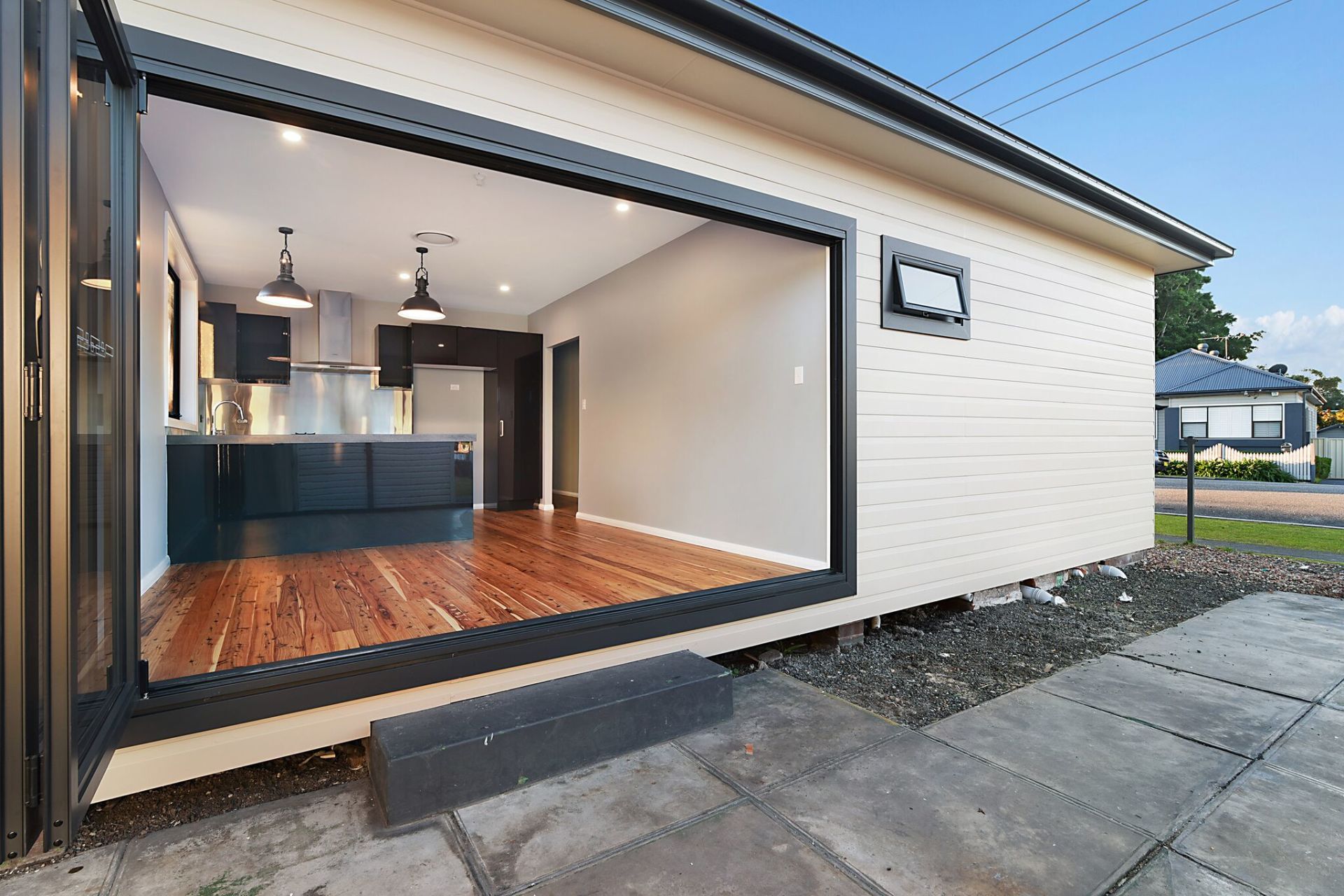 Modern kitchen with open folding doors, wooden floors, and dark cabinets.