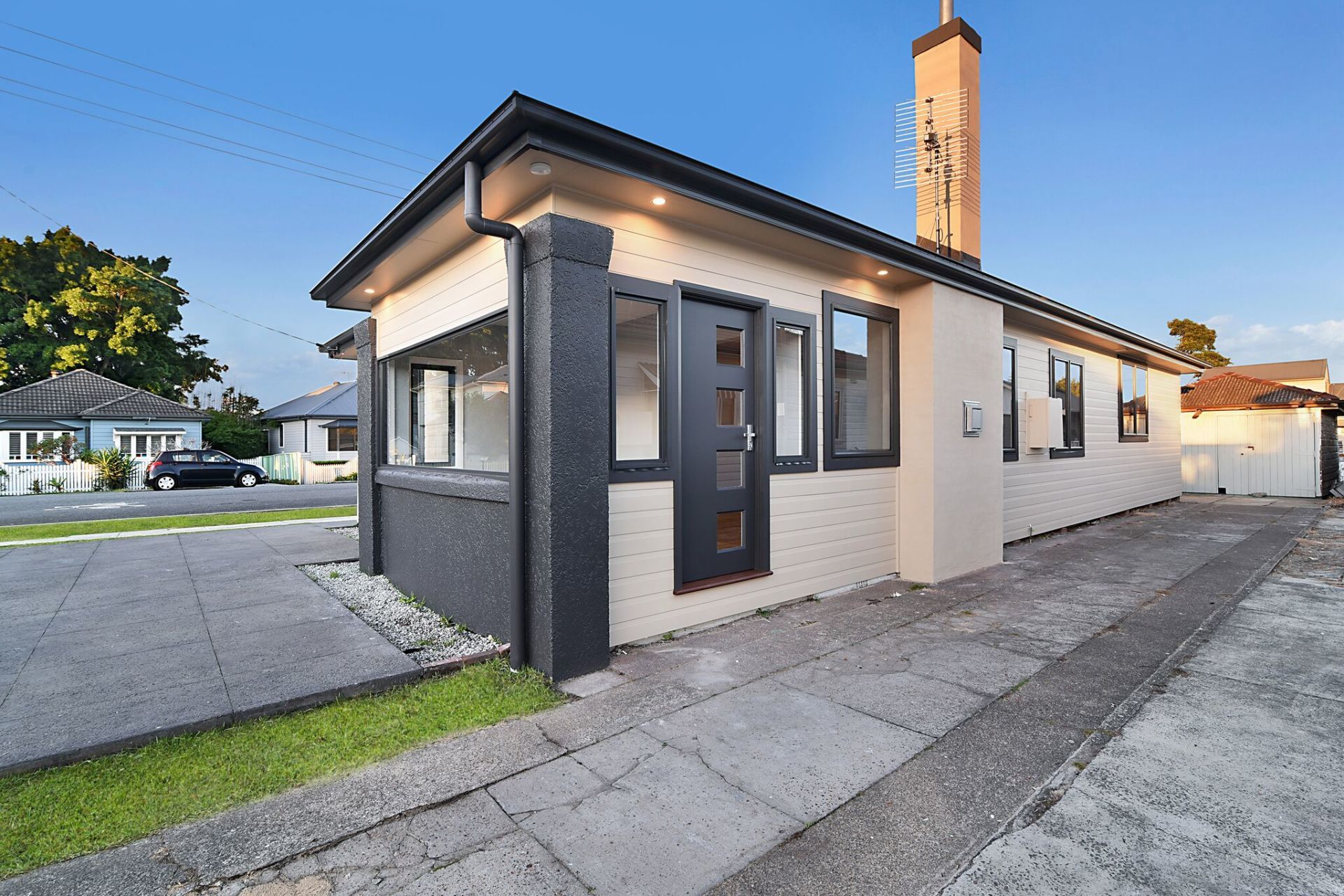 A tan brick bungalow with black trim, front door, and windows. A paved driveway and small lawn.