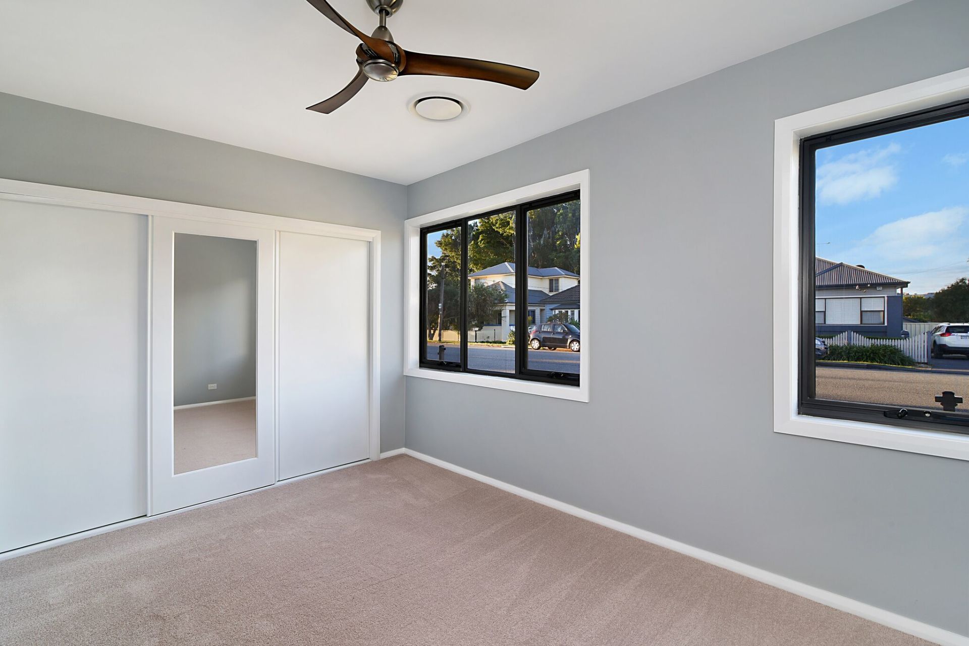 Bedroom with gray walls, mirrored closet doors, windows with black frames, and a ceiling fan.