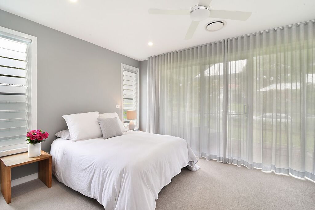 Bedroom with gray walls, white bed, sheer curtains, and a side table with flowers.