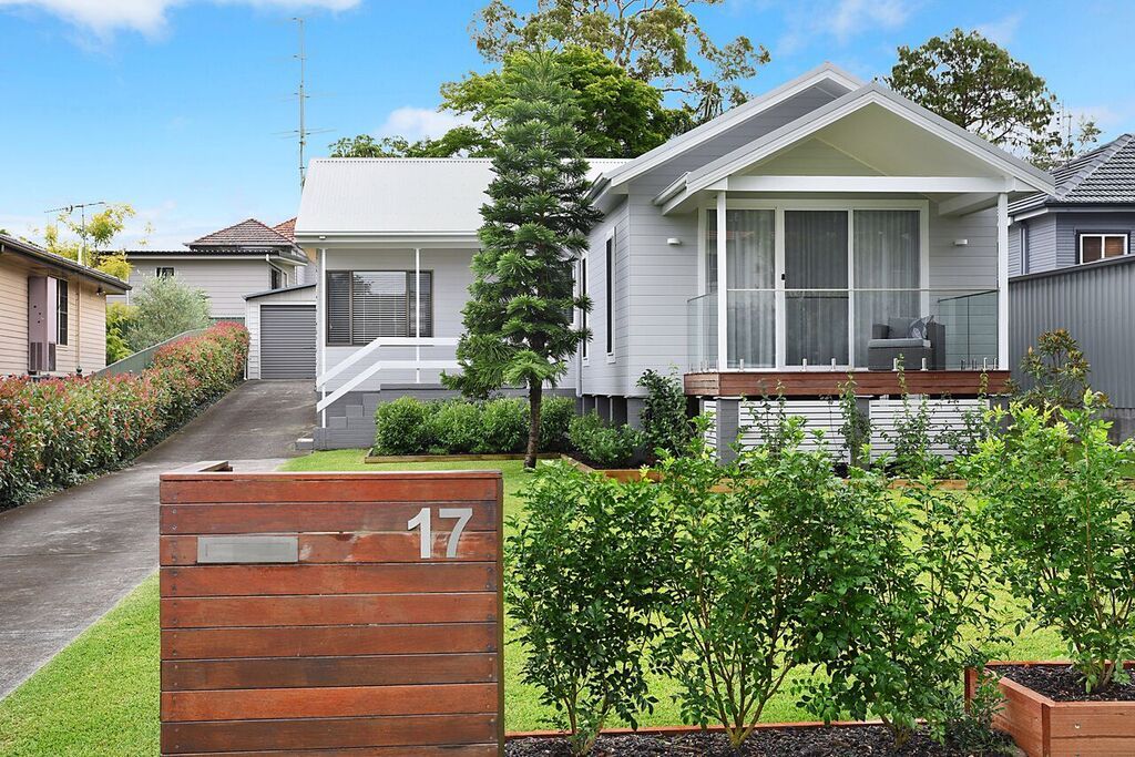 House with wooden fence and number 17, driveway, and landscaping under blue sky.