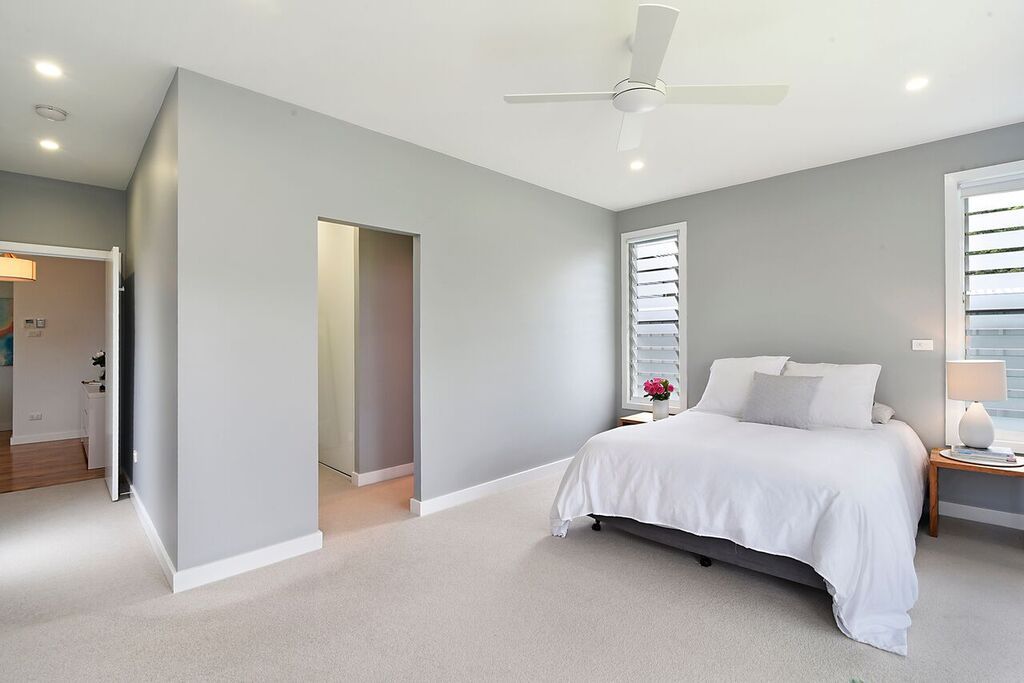 Spacious bedroom with light gray walls, white bedding, a wooden nightstand, and a ceiling fan.
