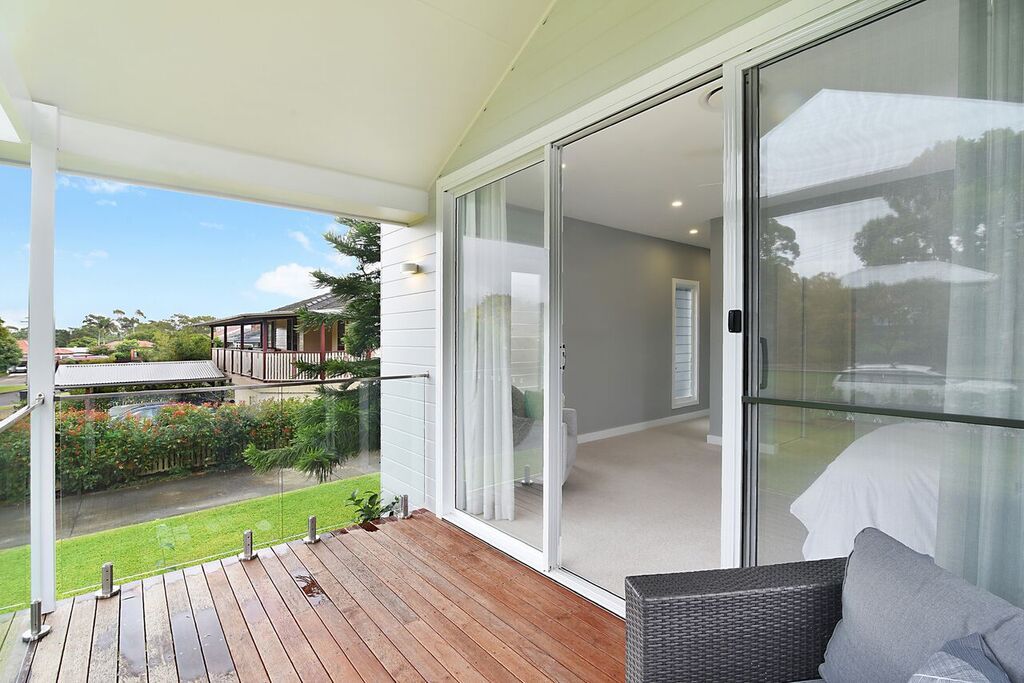 Wooden deck with glass railing overlooking a landscaped area. Sliding glass door leads to a bedroom.