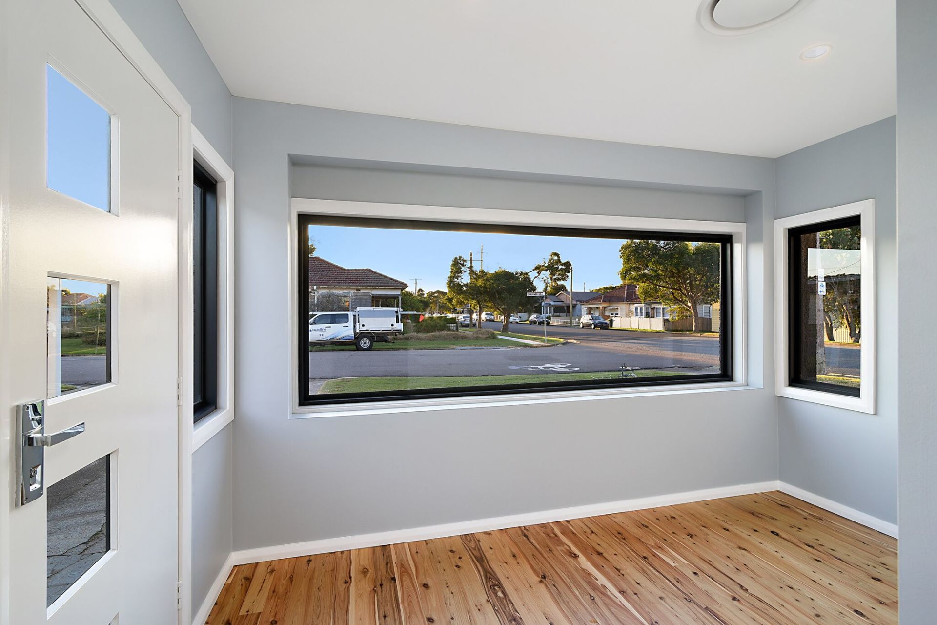 Interior view of room with large window overlooking suburban street, hardwood floor, blue-gray walls.