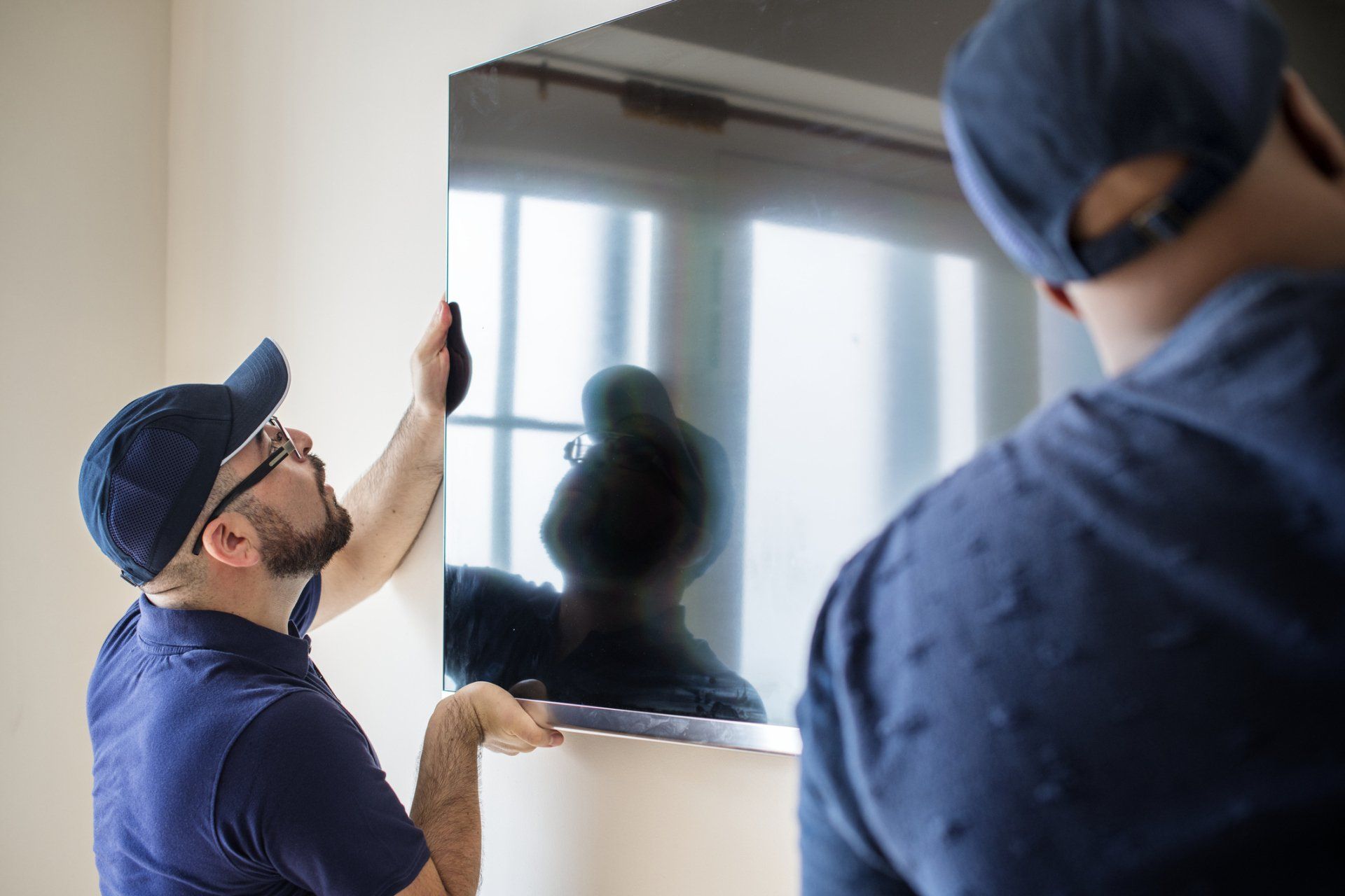 Two workers in blue uniforms installing a wall-mounted TV in a bright room
