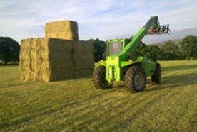 A green tractor next to bales of hay in a field