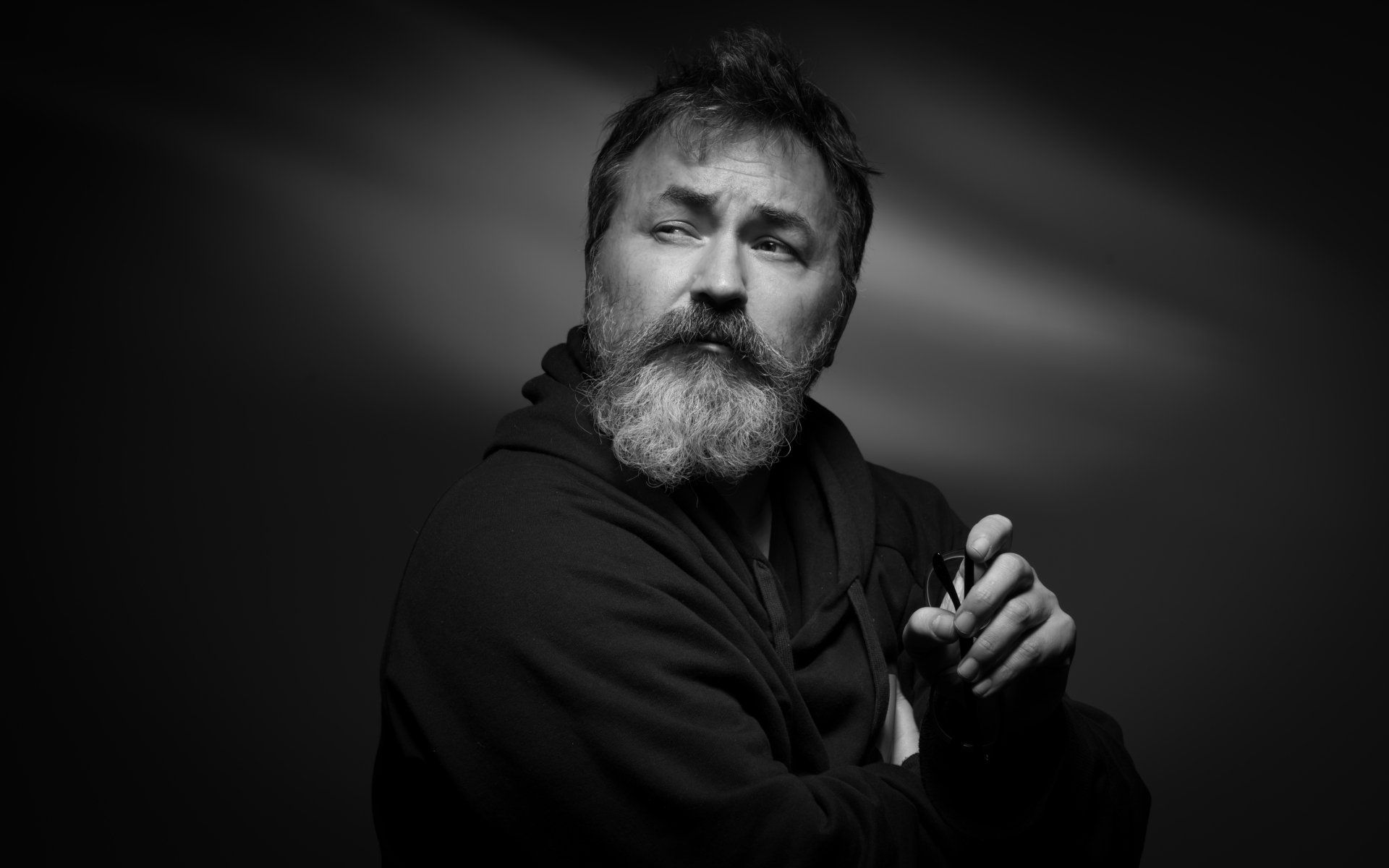 dramatic black and white portrait of a man with a thick beard and moustache looking over his shoulder