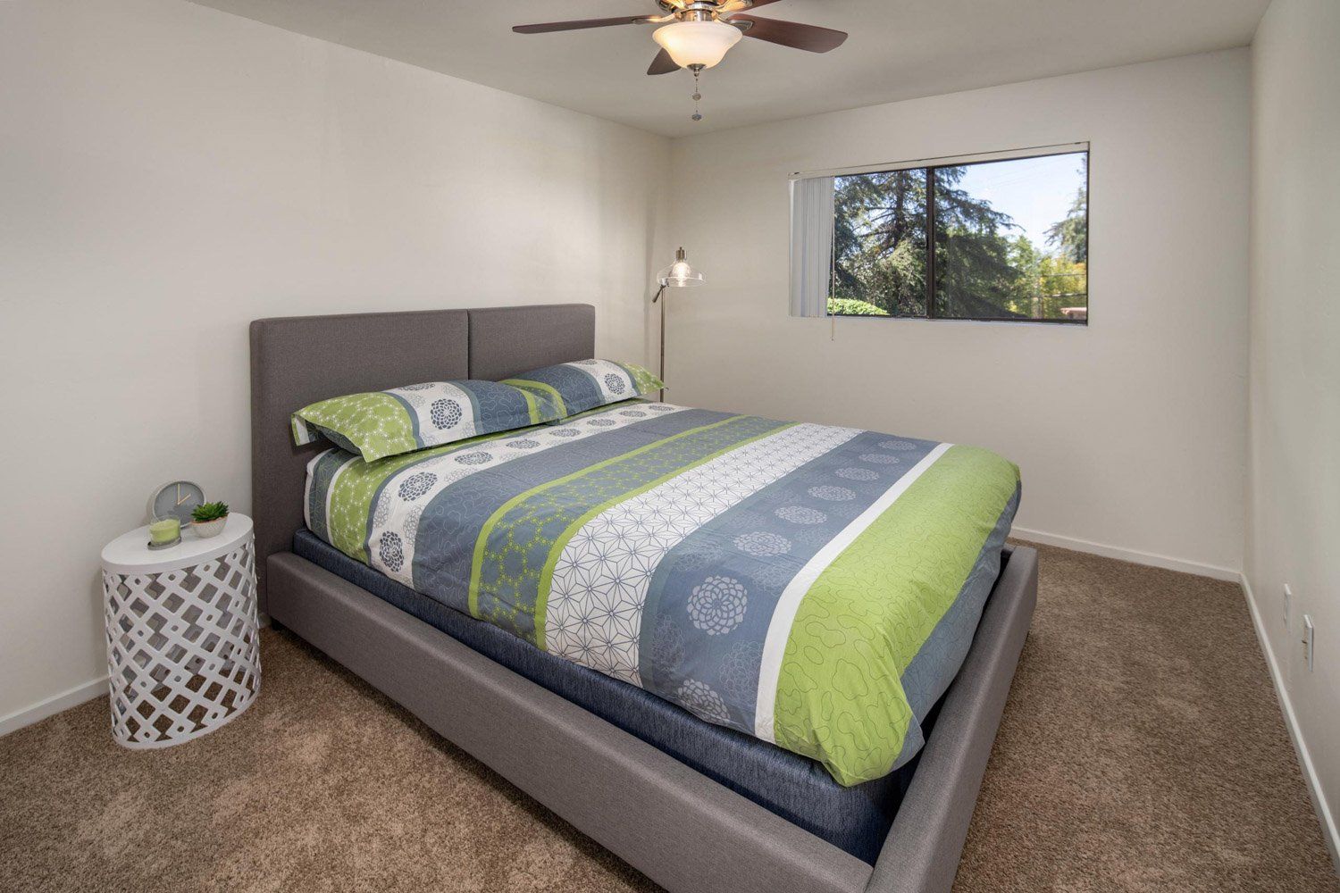 A bedroom with a bed , nightstand , lamp and ceiling fan.