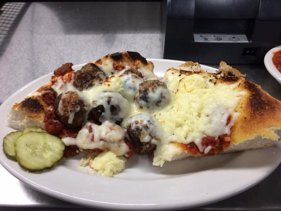 A white plate topped with a slice of meatball pizza and pickles.