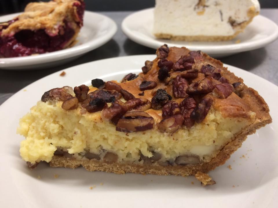A slice of pie with pecans on top on a white plate