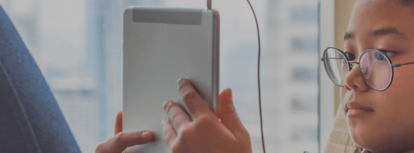 Una persona con gli occhiali usa un tablet argentato, vista di profilo contro uno sfondo di finestre.