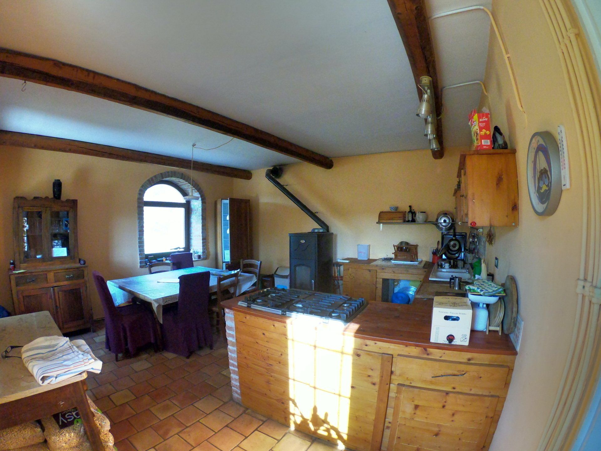 Una cucina e zona pranzo rustica con travi in ​​legno a vista, un'isola centrale in legno, un tavolo da pranzo e pavimenti in cotto.