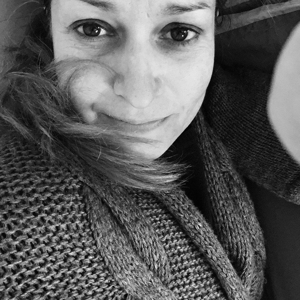 Un primo piano in bianco e nero di una persona con i capelli che le coprono parzialmente il viso, che guarda in camera.